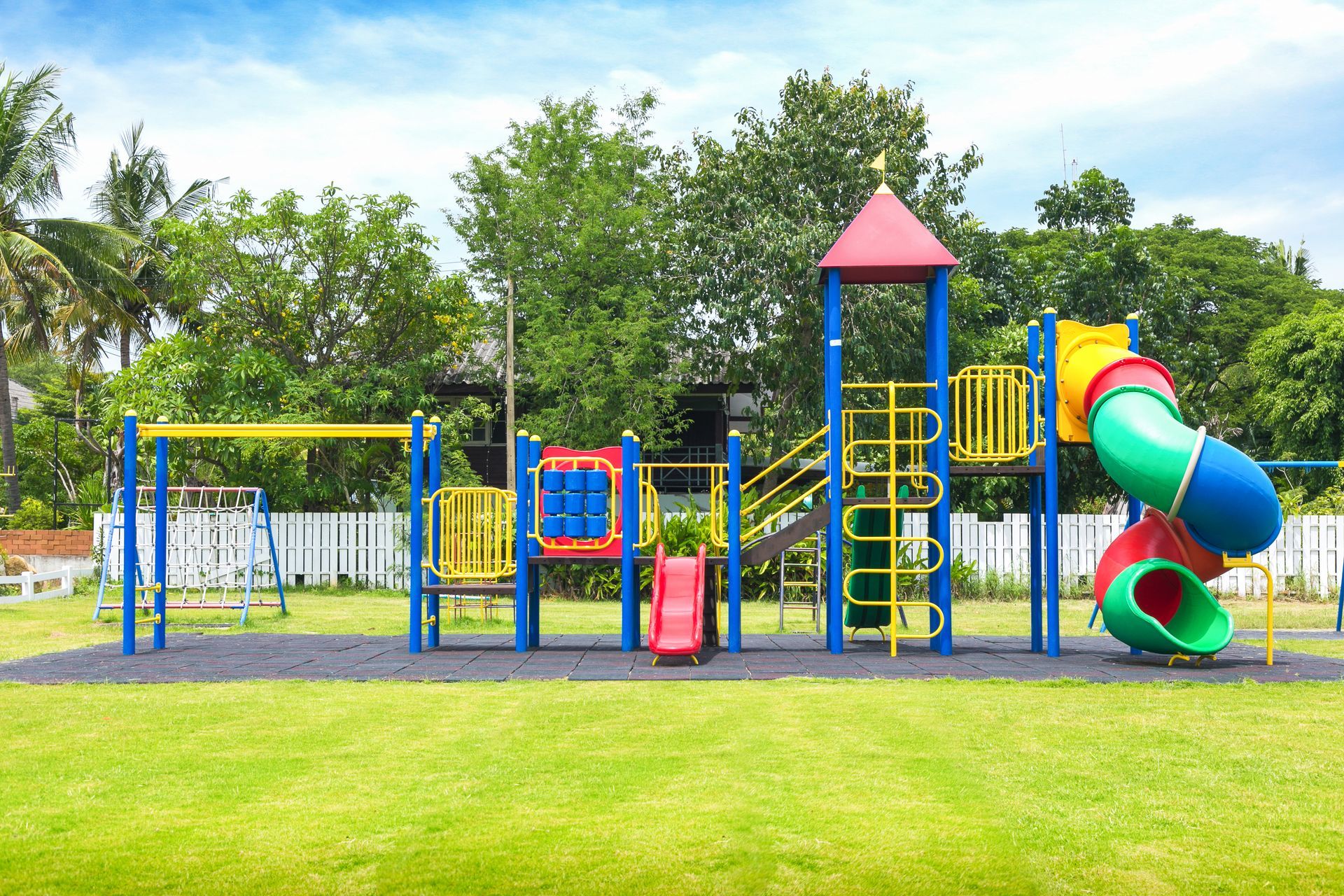 Colorful outdoor playground equipment with slides, a climbing net, and a central tower on a grassy lawn.