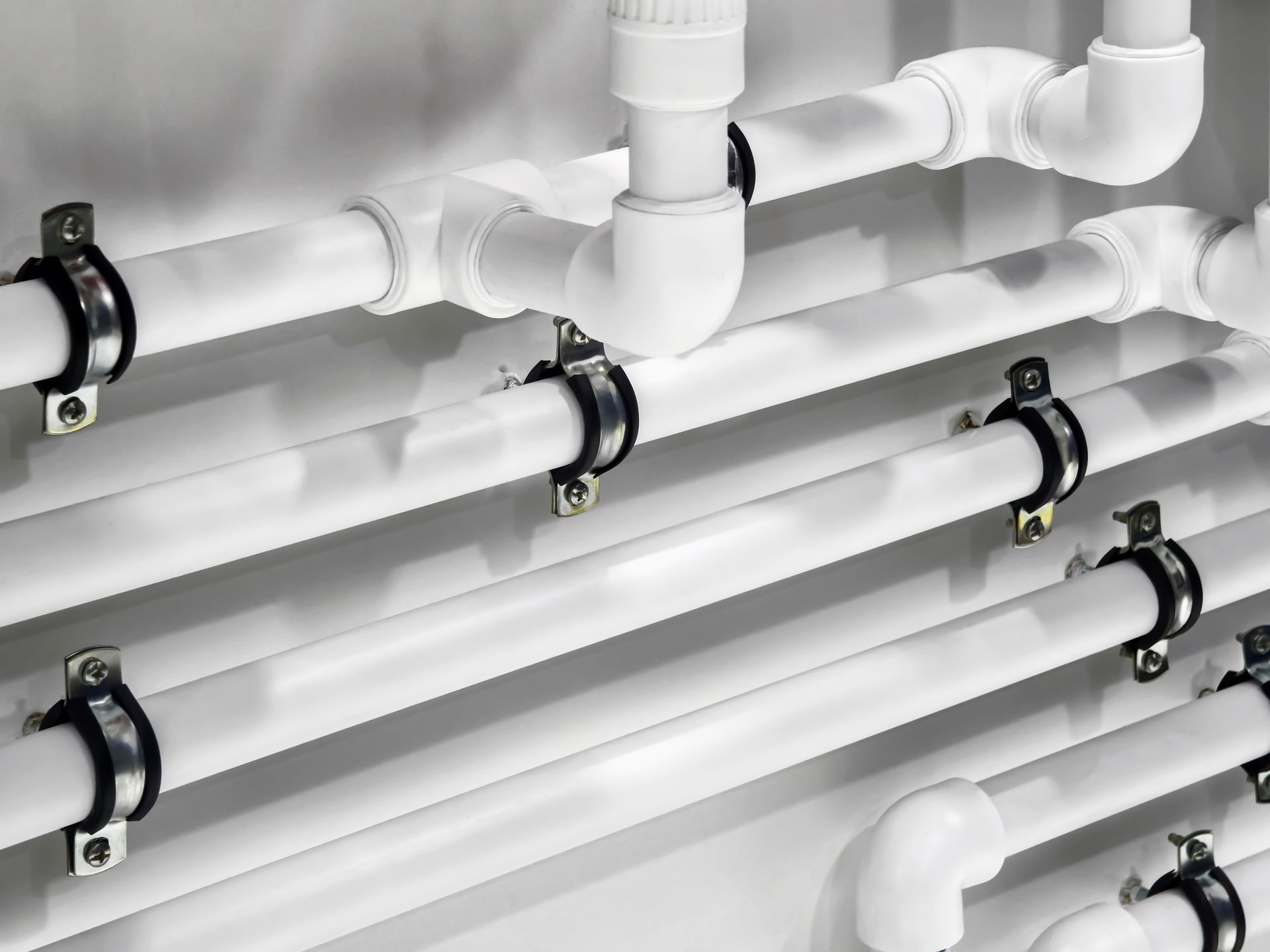 White plastic pipes secured with metal mounting brackets against a plain background.