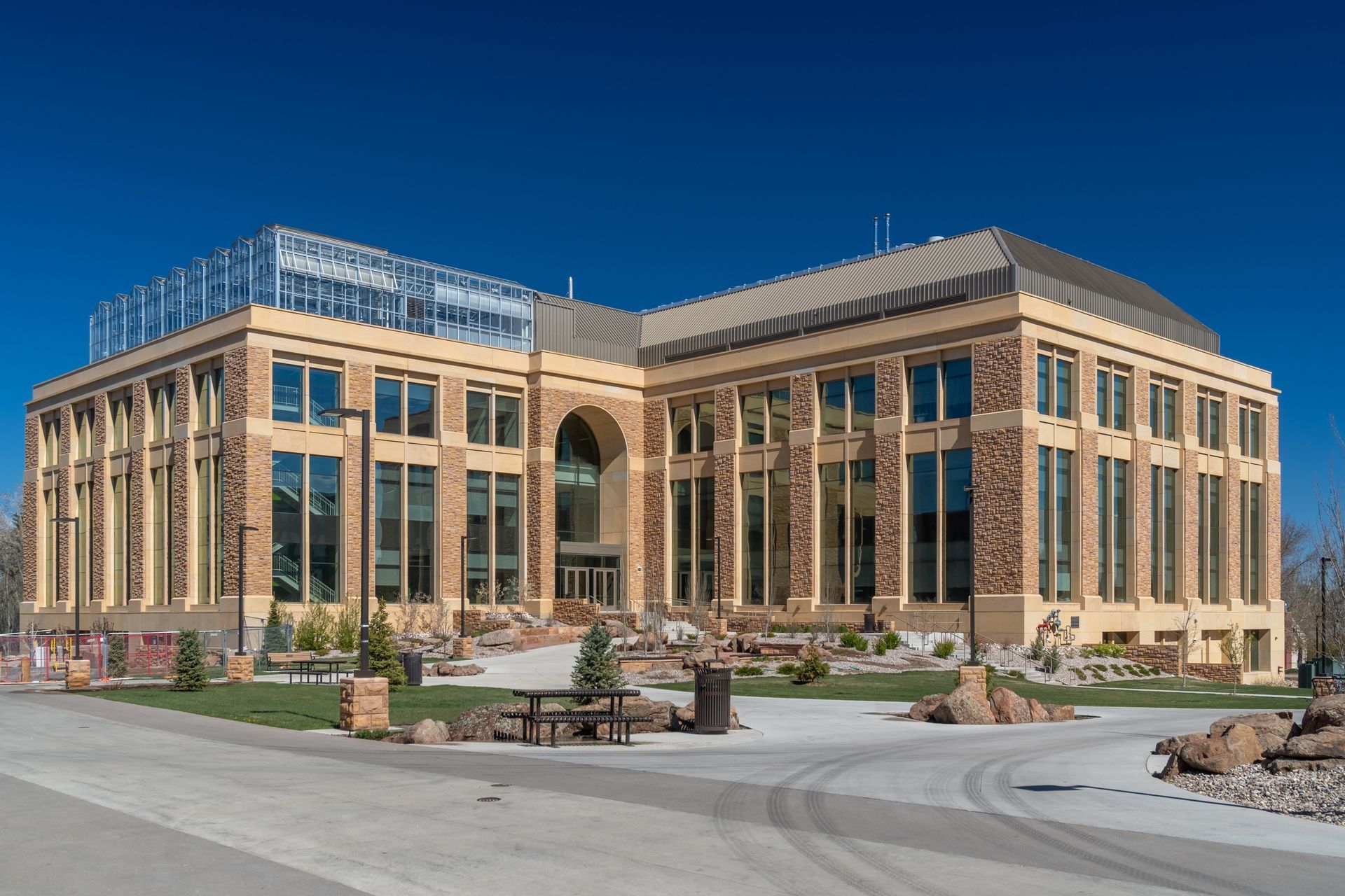 A three-story building with stone-accented facade, large windows, and a central archway entrance under a clear blue sky.