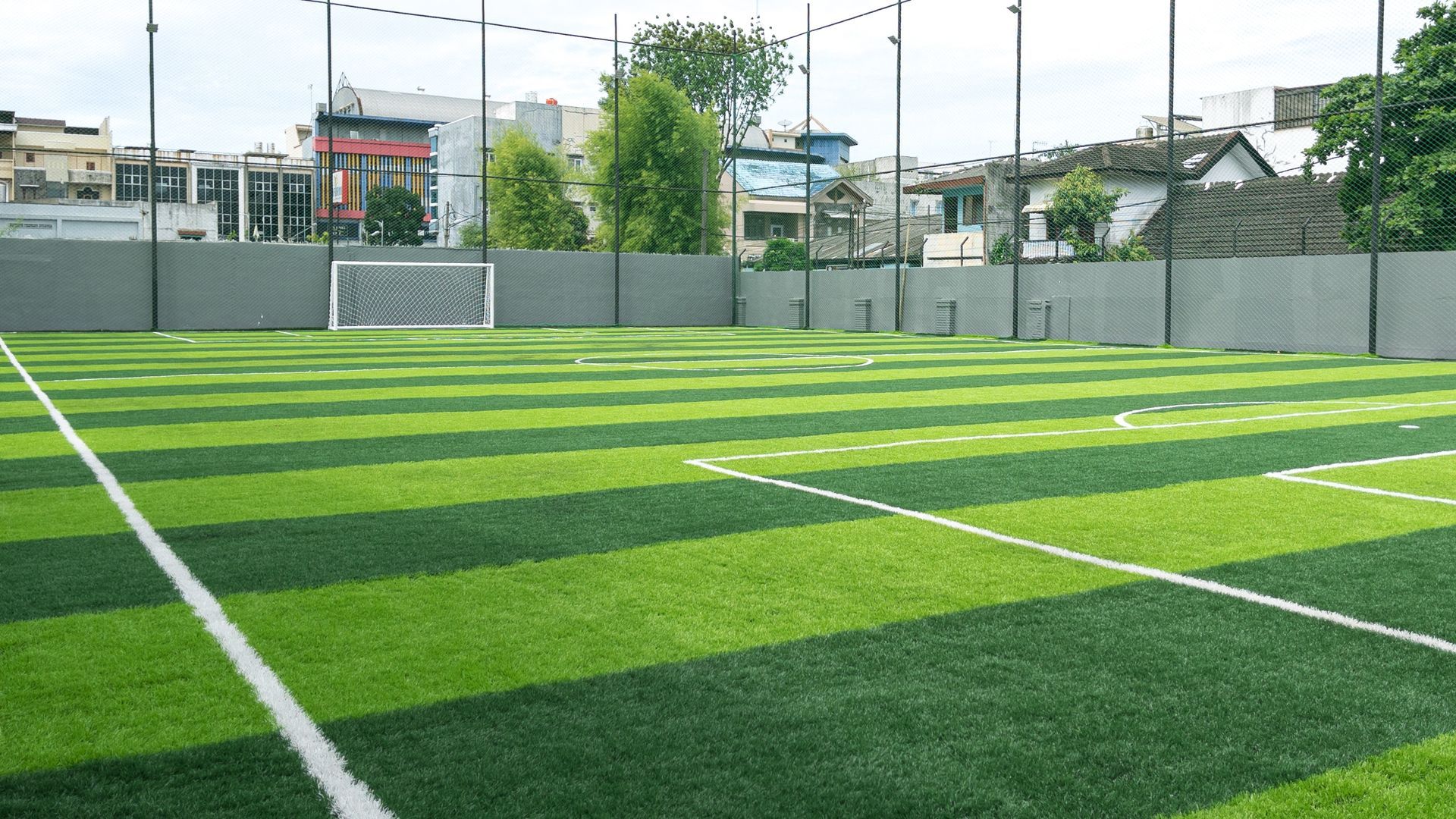 An outdoor soccer field with light and dark green striped artificial turf, white boundary lines, and a goal net.