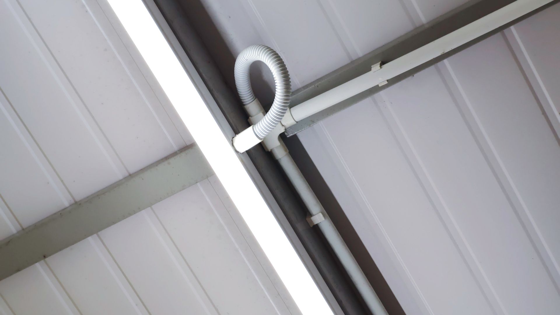 A white conduit pipe with a looped flexible section attached to a metal ceiling beam.