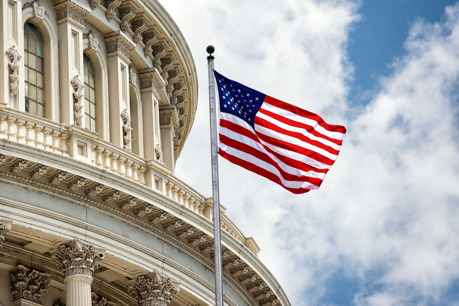 The American flag waving on a pole in front of the white, domed architecture of the United States Capitol building.