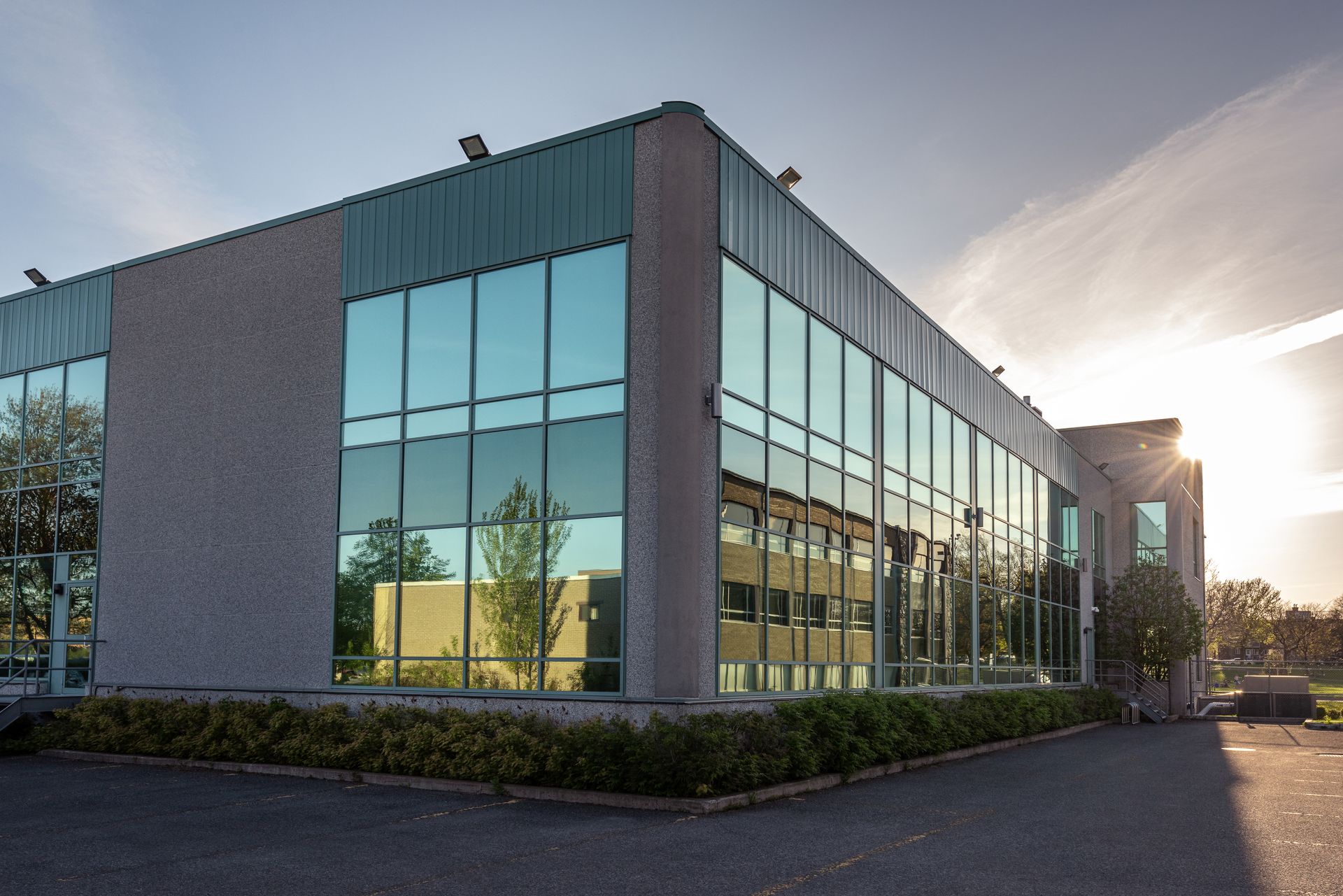 A modern, two-story commercial office building with glass curtain walls and concrete corners at sunset.