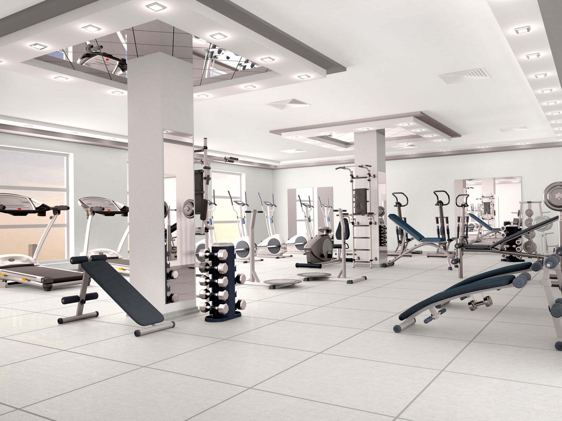 A modern, bright indoor gym with rows of treadmills, benches, and a rack of dumbbells set against white walls.