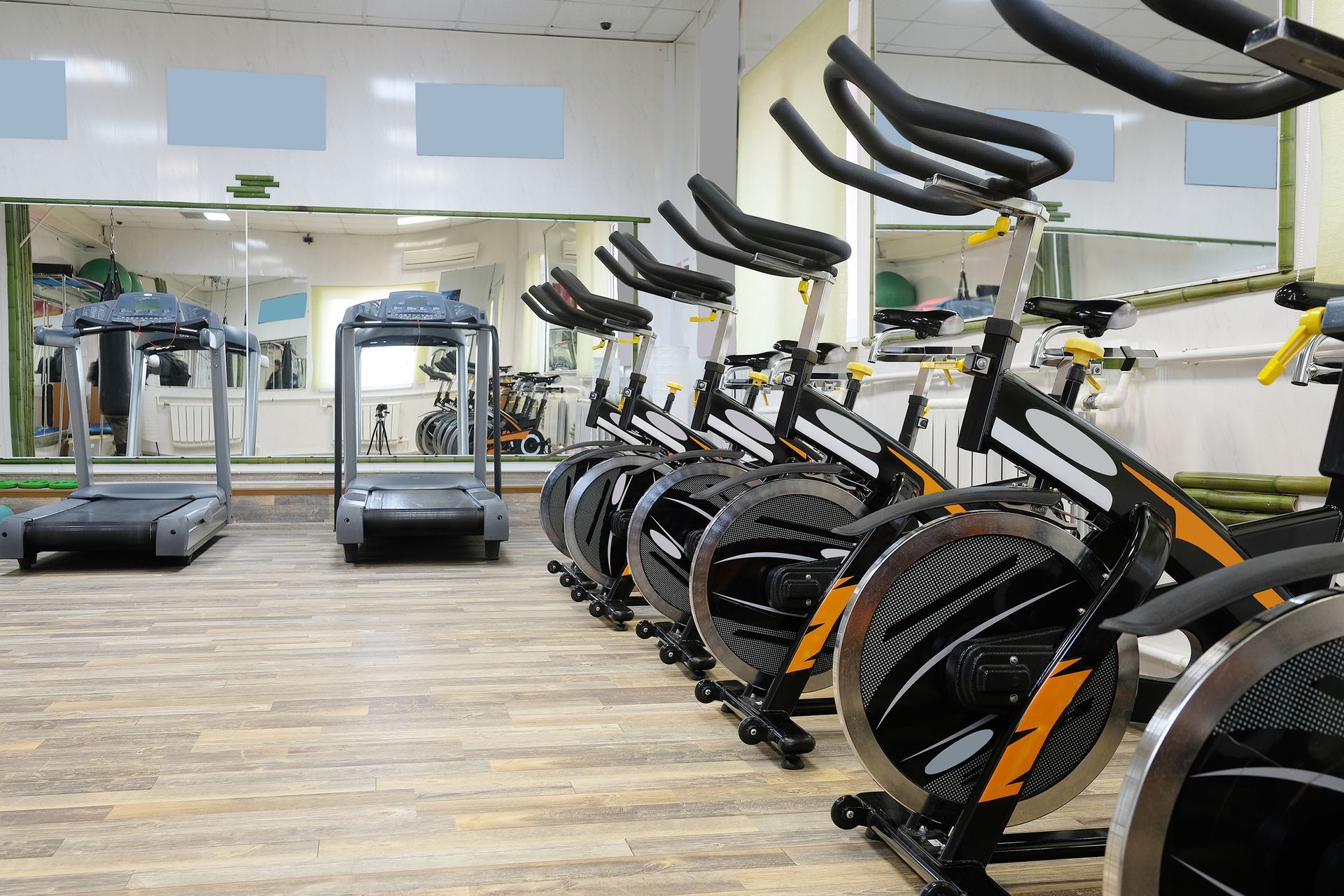 A row of black and yellow stationary bikes in a gym, with two treadmills visible in the background reflecting in a mirror.
