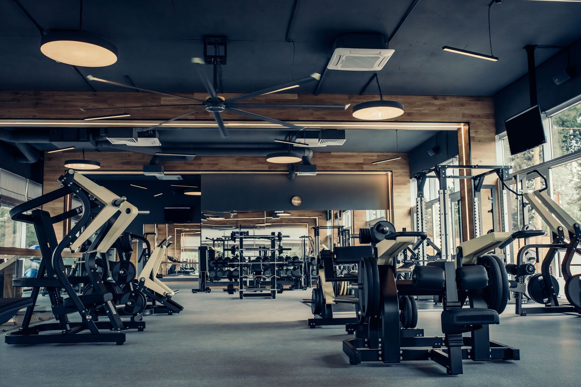 Modern gym interior with various workout machines, dark ceilings, and wood-paneled walls.