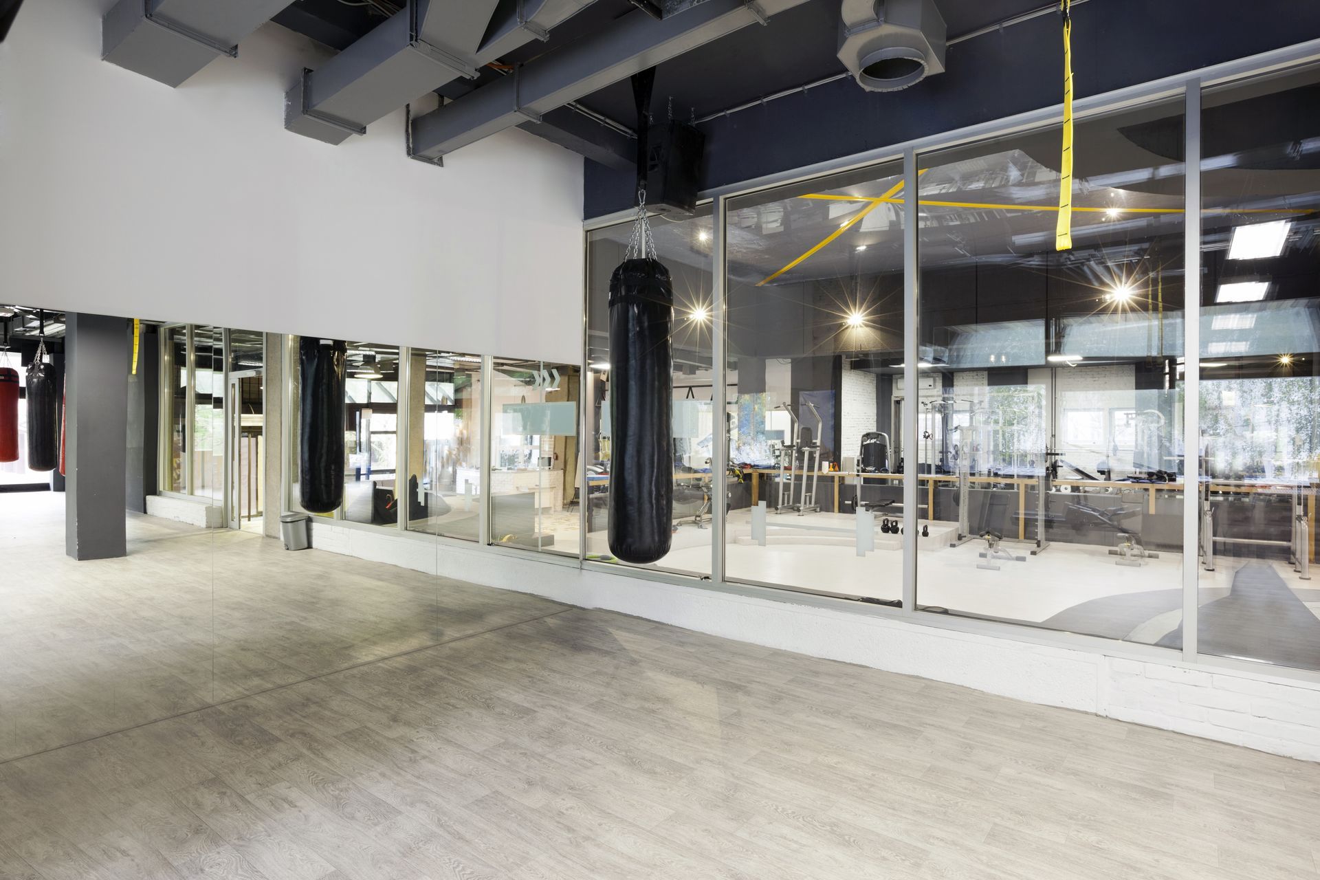 A spacious, modern gym interior featuring polished concrete floors, a wall mirror, and a hanging black boxing heavy bag.