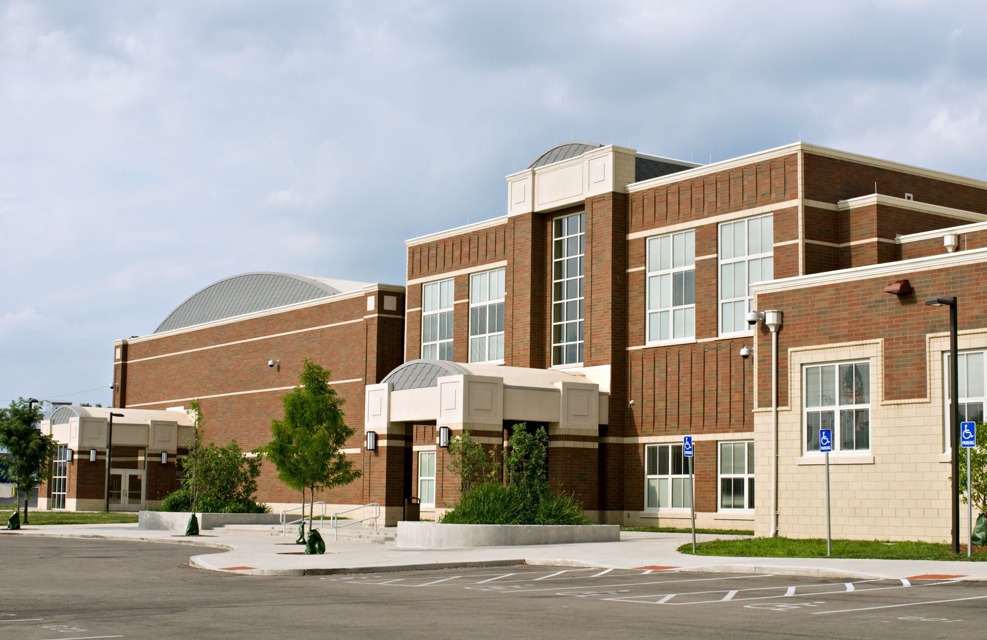 A modern, two-story brick building with a curved roof, a central entrance, and a parking lot in the foreground.