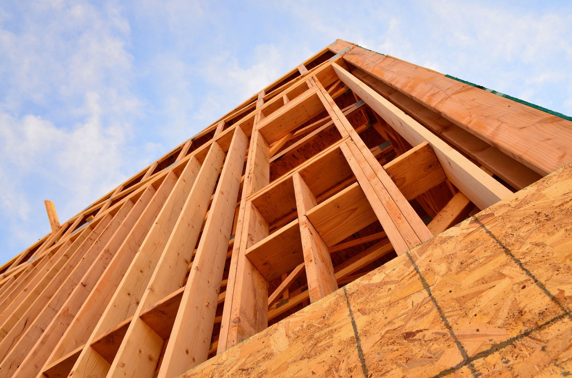 A low-angle view of the wooden frame of a building under construction against a partly cloudy blue sky.