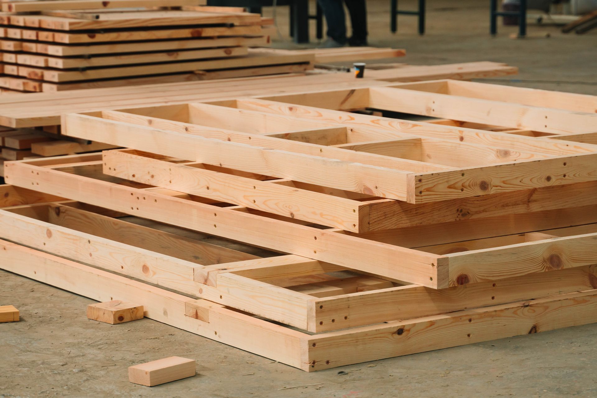 A stack of pre-fabricated wooden wall frames sitting on a concrete floor in a workshop.