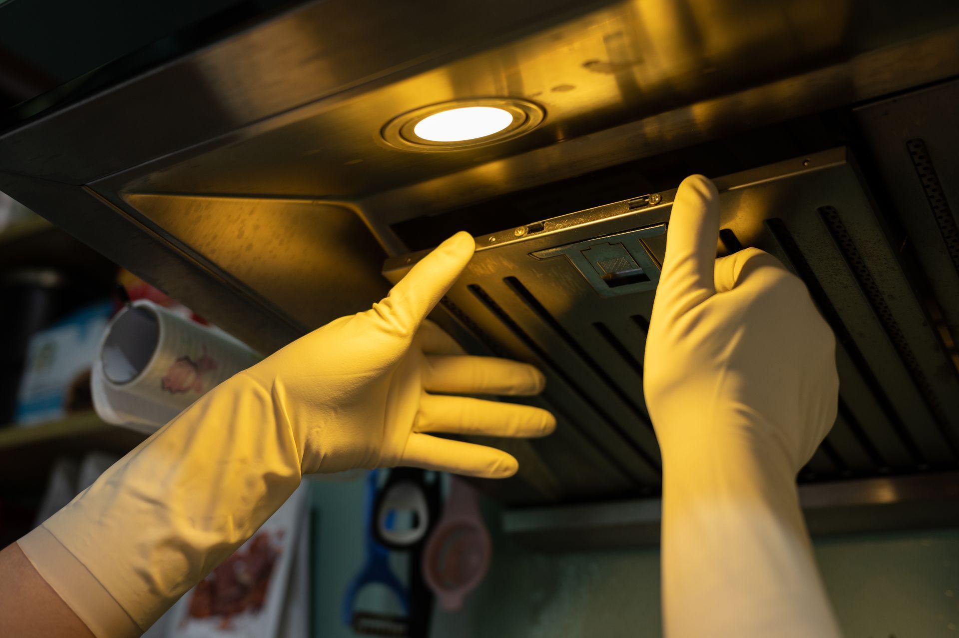 A person wearing yellow rubber gloves cleaning a kitchen range hood filter.