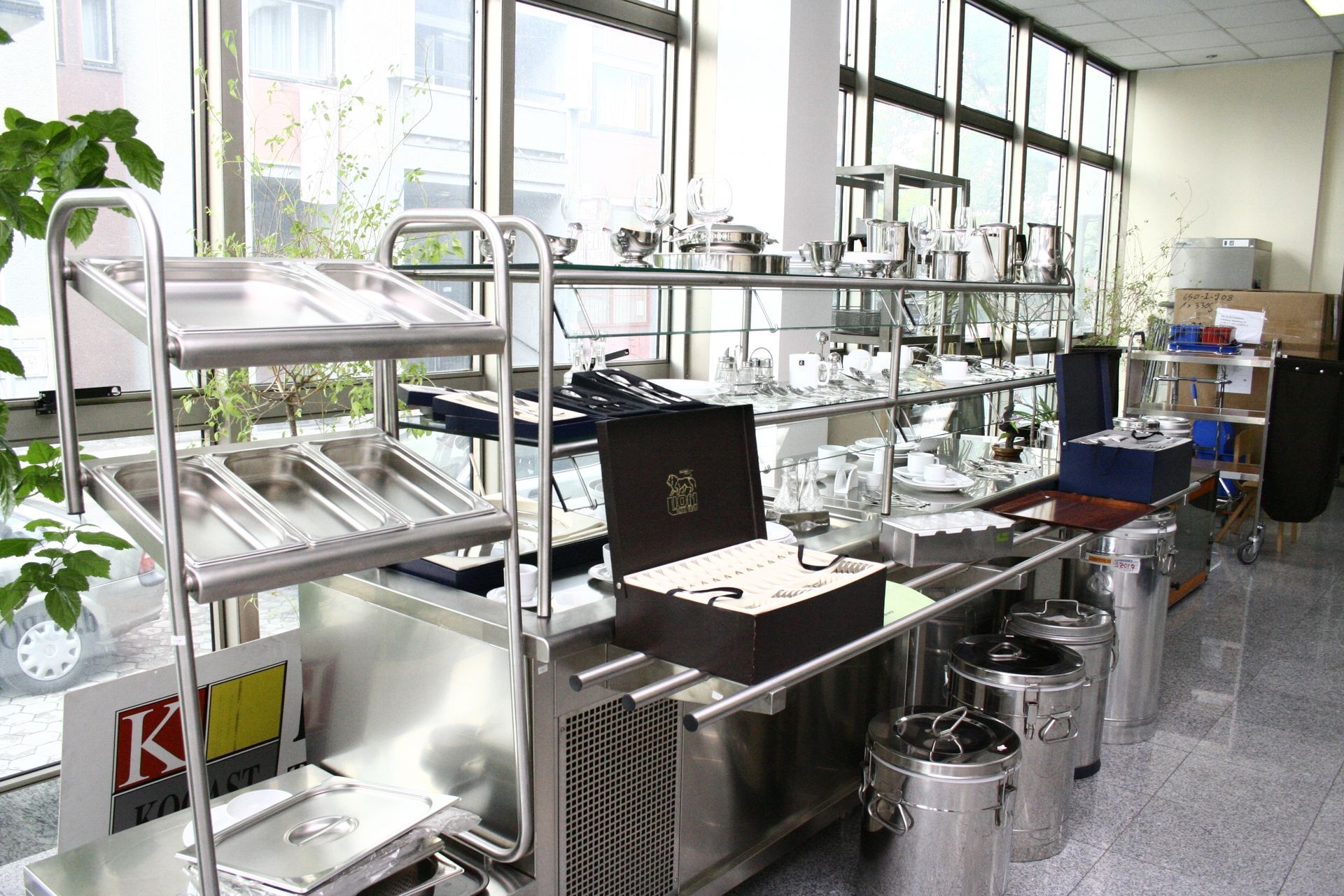 Stainless steel kitchen catering equipment, including tiered racks and storage containers, in a bright showroom setting.