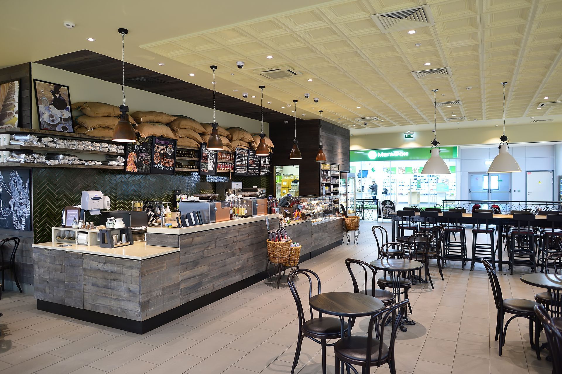 An indoor coffee shop with a wooden service counter, menu boards, coffee bean bags, and seating for customers.