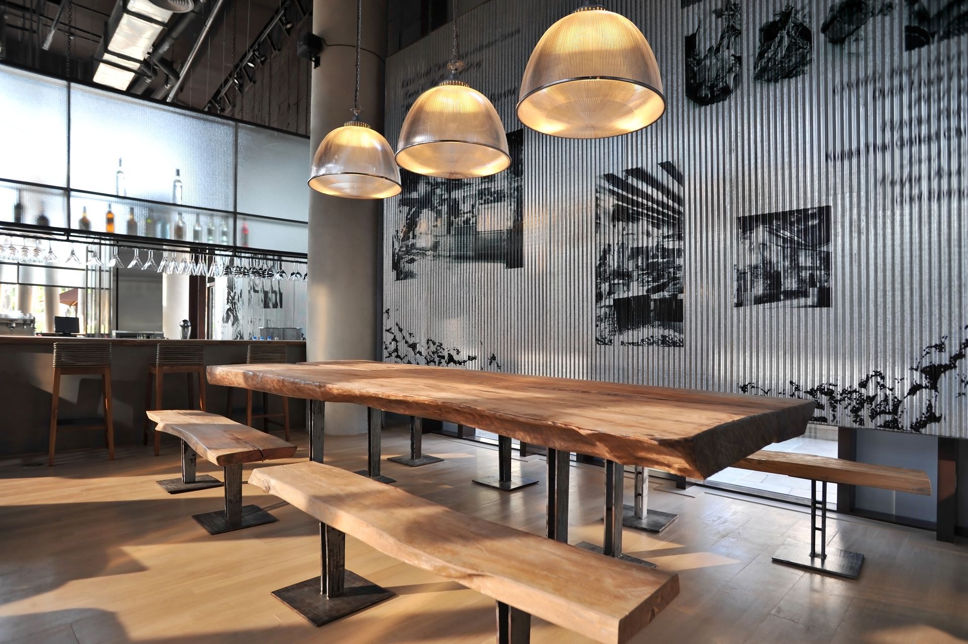 Modern dining area featuring a long live-edge wooden table with benches under three hanging pendant lights.