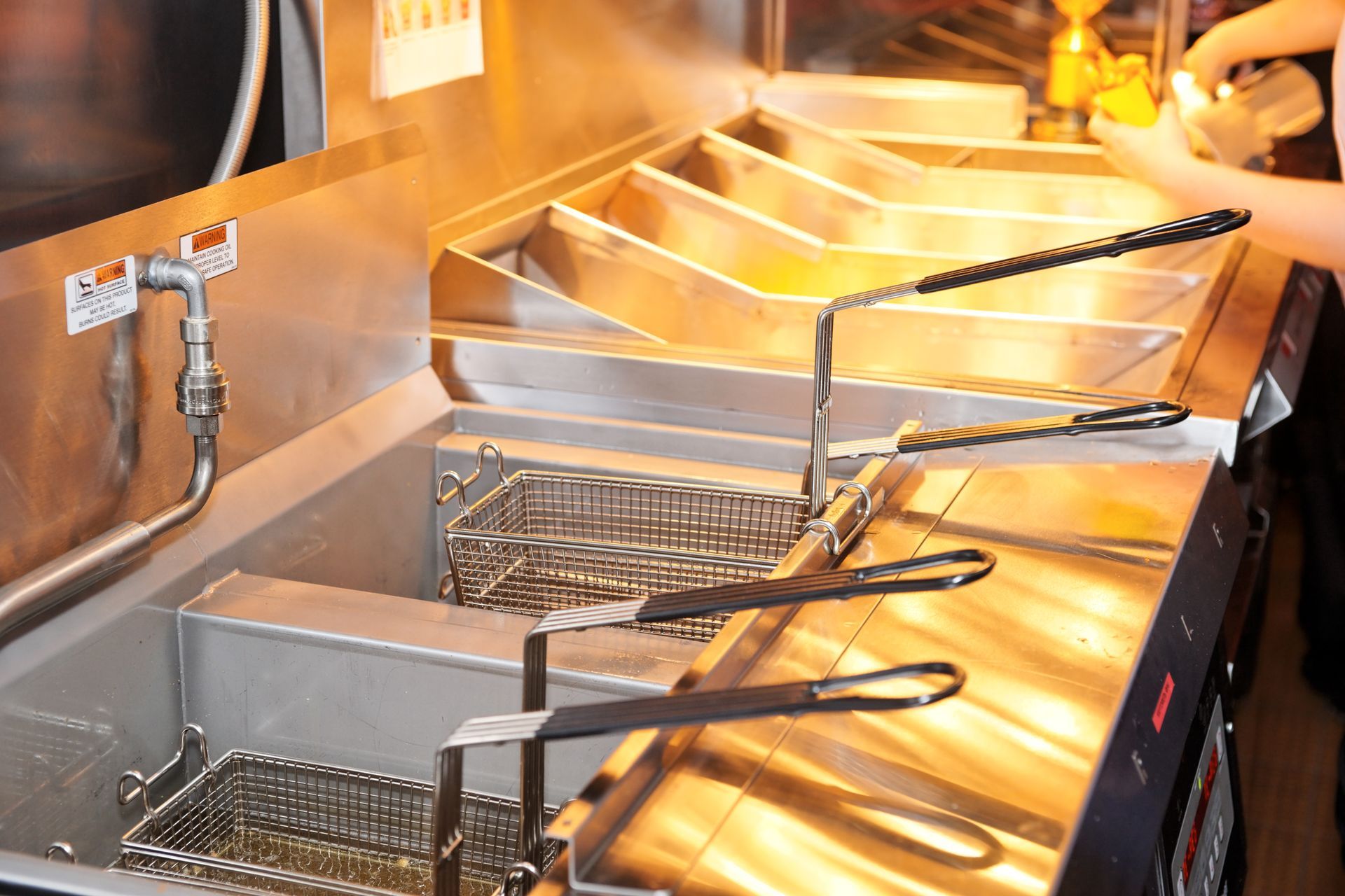 A commercial deep fryer station with multiple metal vats and wire baskets in a restaurant kitchen.
