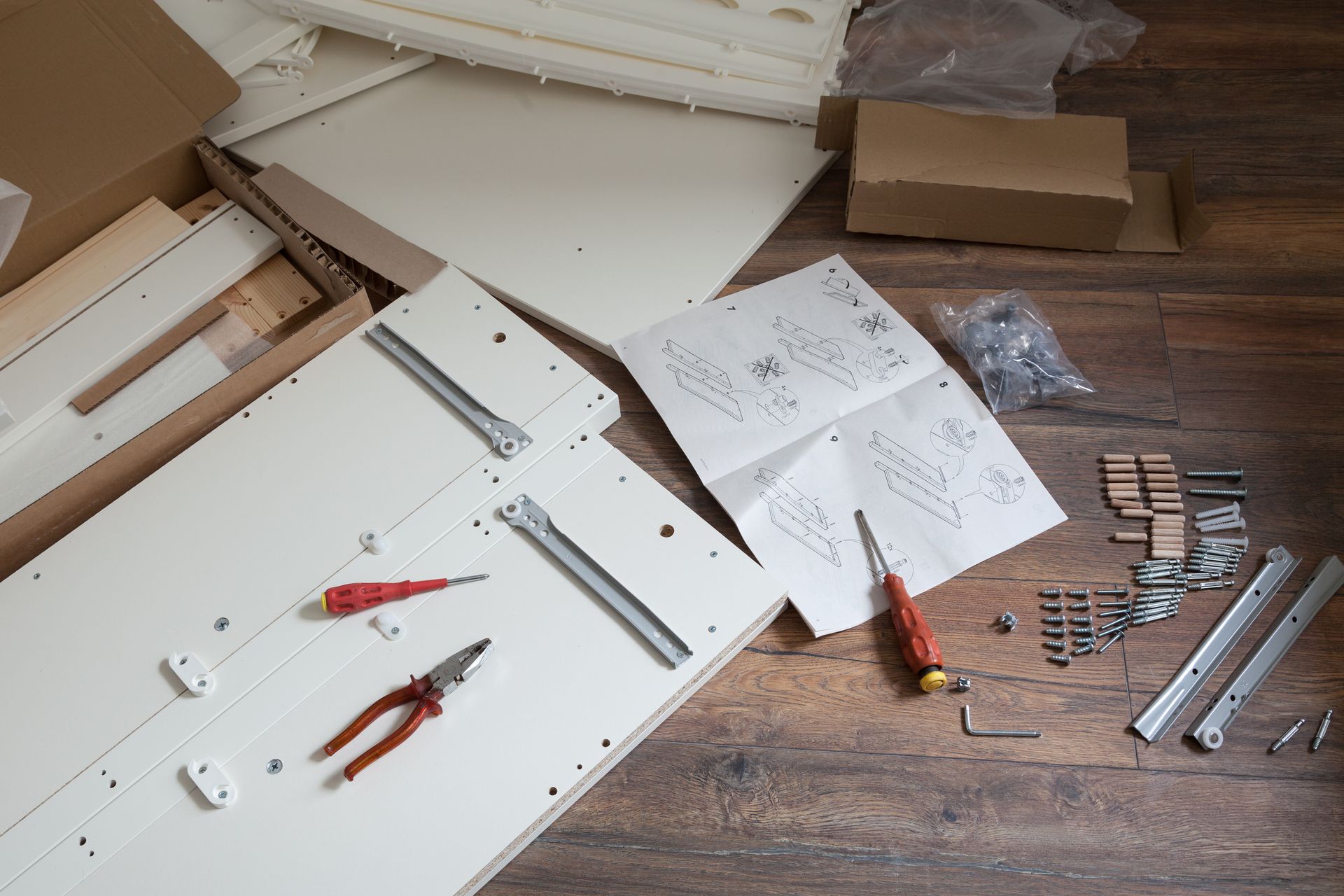 Furniture parts and hardware for assembly spread across a wooden floor, with instruction manuals and tools nearby.