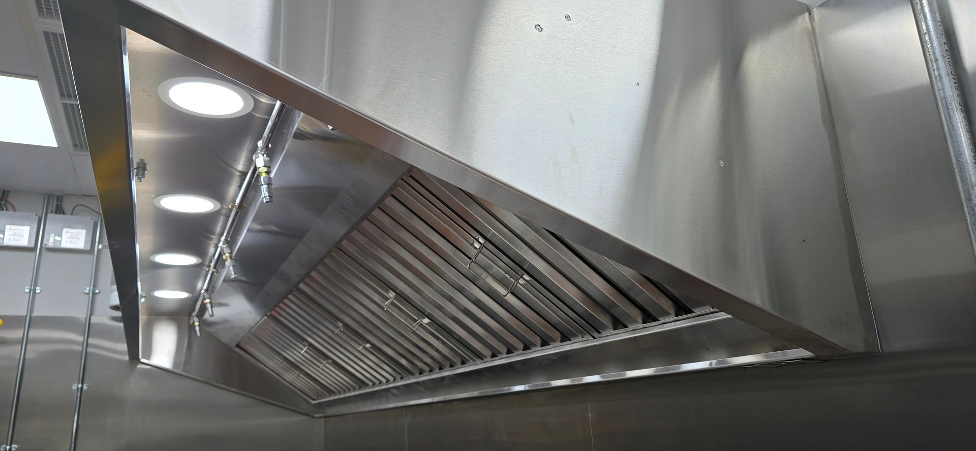 A stainless steel commercial kitchen exhaust hood with integrated lighting and metal baffle grease filters.