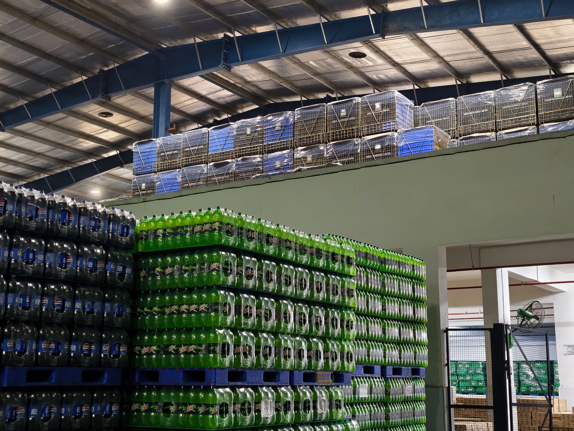 Stacks of green-labeled plastic bottles on blue pallets in a large, industrial warehouse.