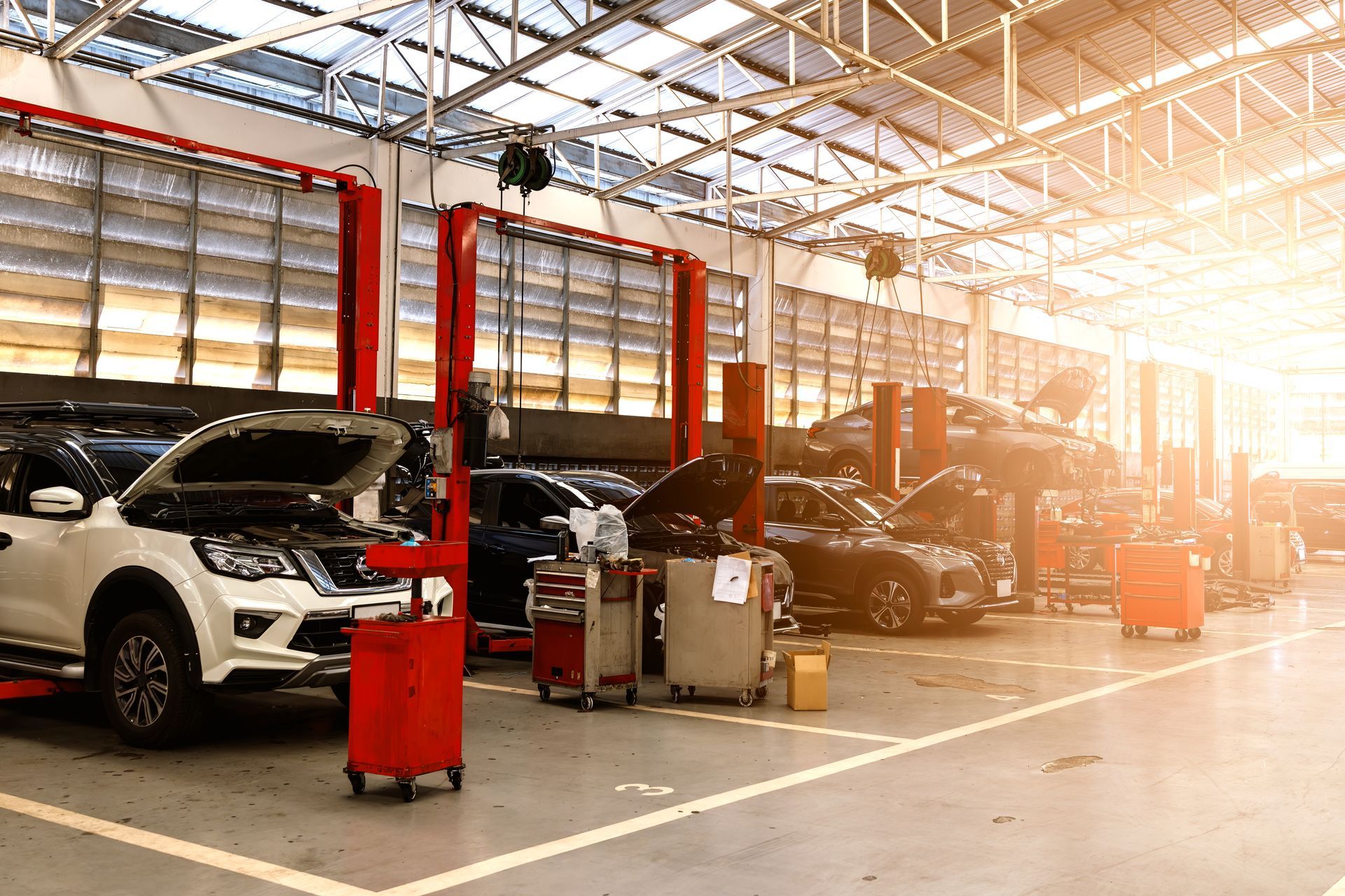 A sunlit automotive service center featuring several cars with open hoods parked in bays for maintenance.