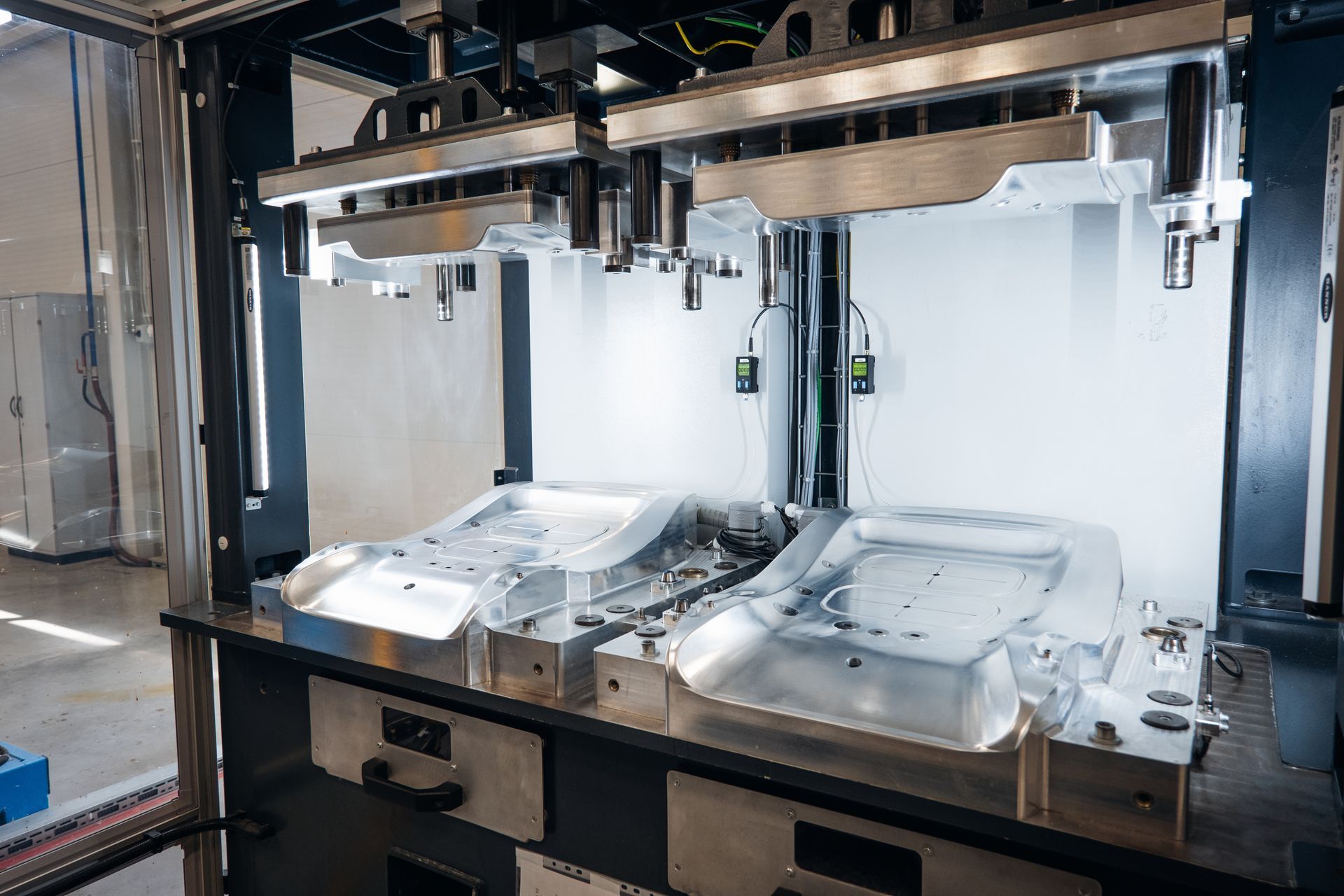 Industrial metal molding machine with two open, silver-colored molds in a brightly lit factory setting.