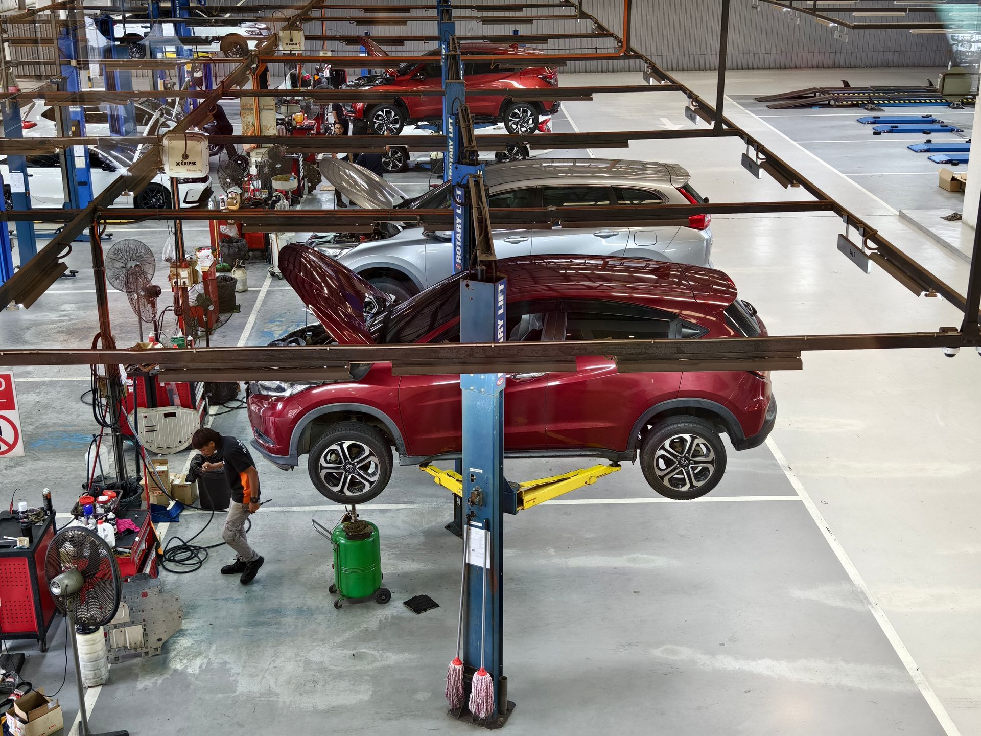 A technician works on a raised red SUV in a brightly lit automotive repair shop with multiple service bays.