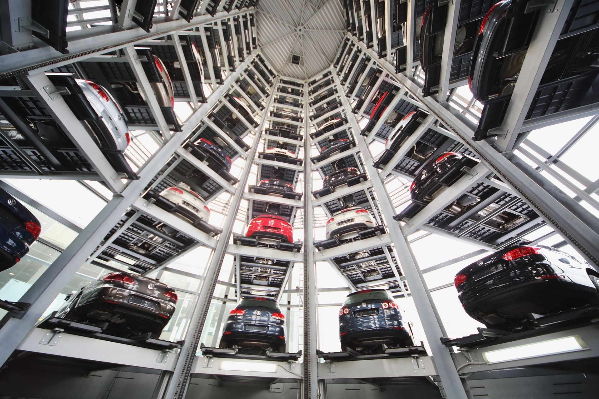 Automated glass tower parking garage containing rows of parked cars on multiple levels, viewed from below.