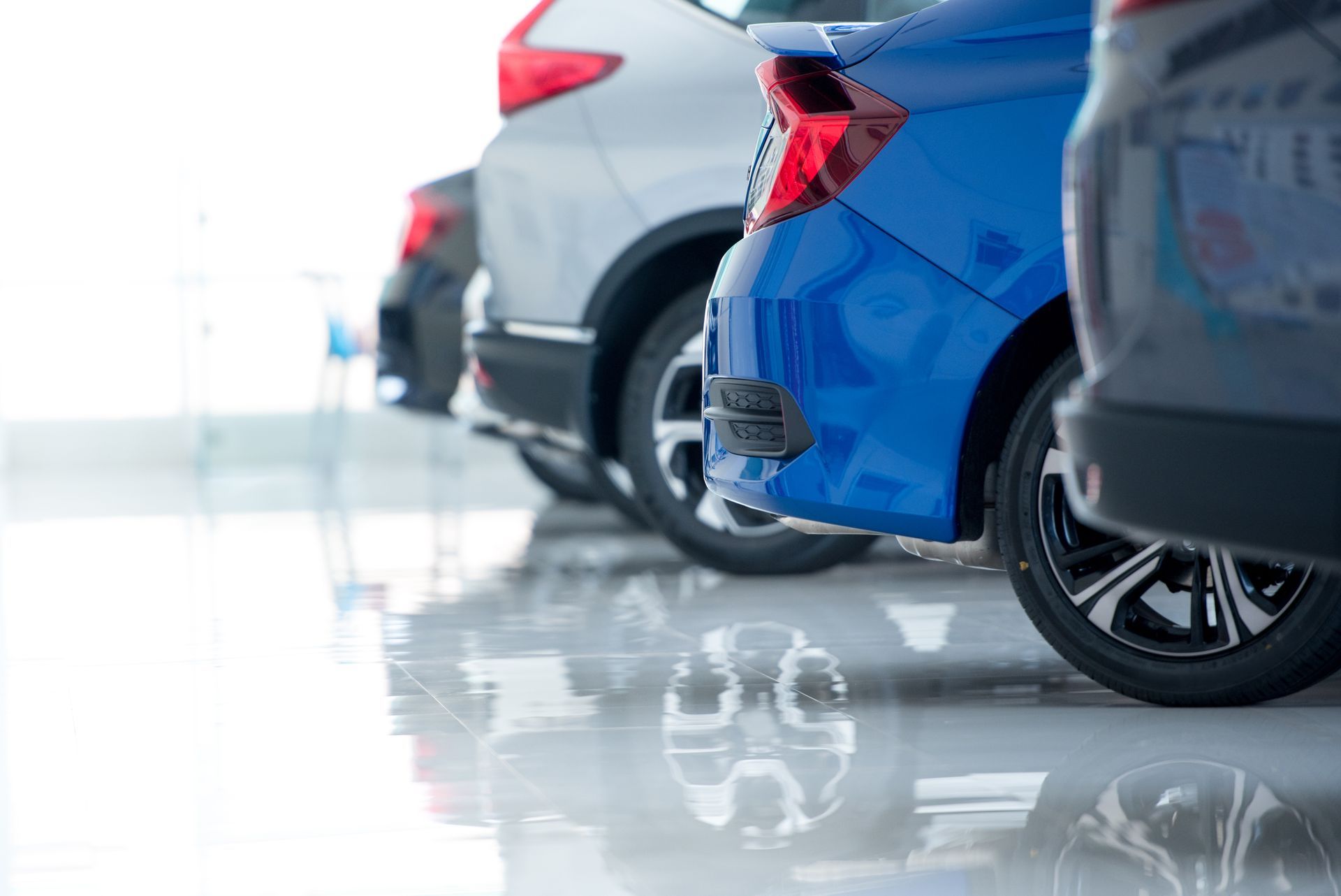 A row of cars, including a prominent blue sedan, parked on a reflective floor in a brightly lit showroom.