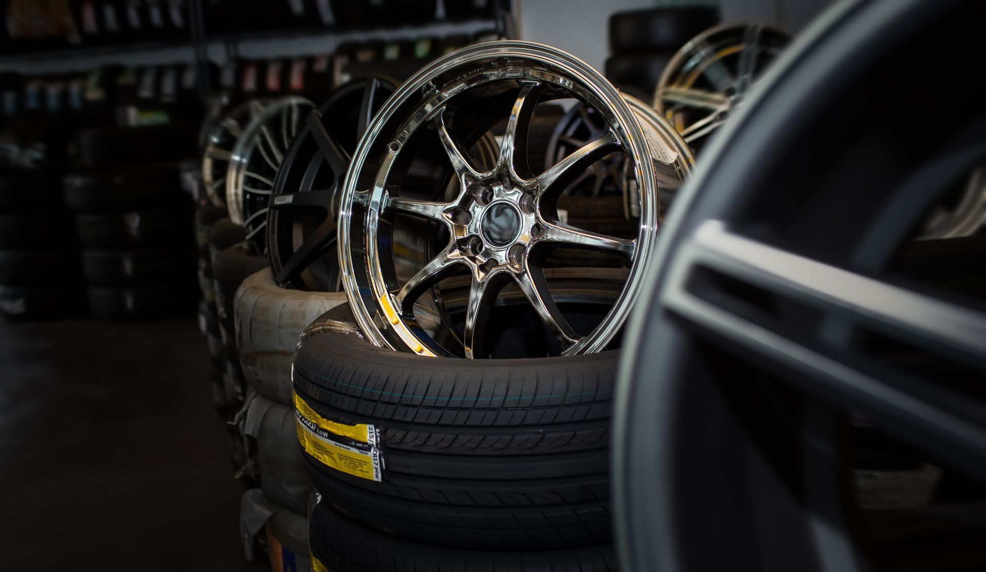A stack of black tires topped with a shiny, chrome multi-spoke wheel in a tire shop.