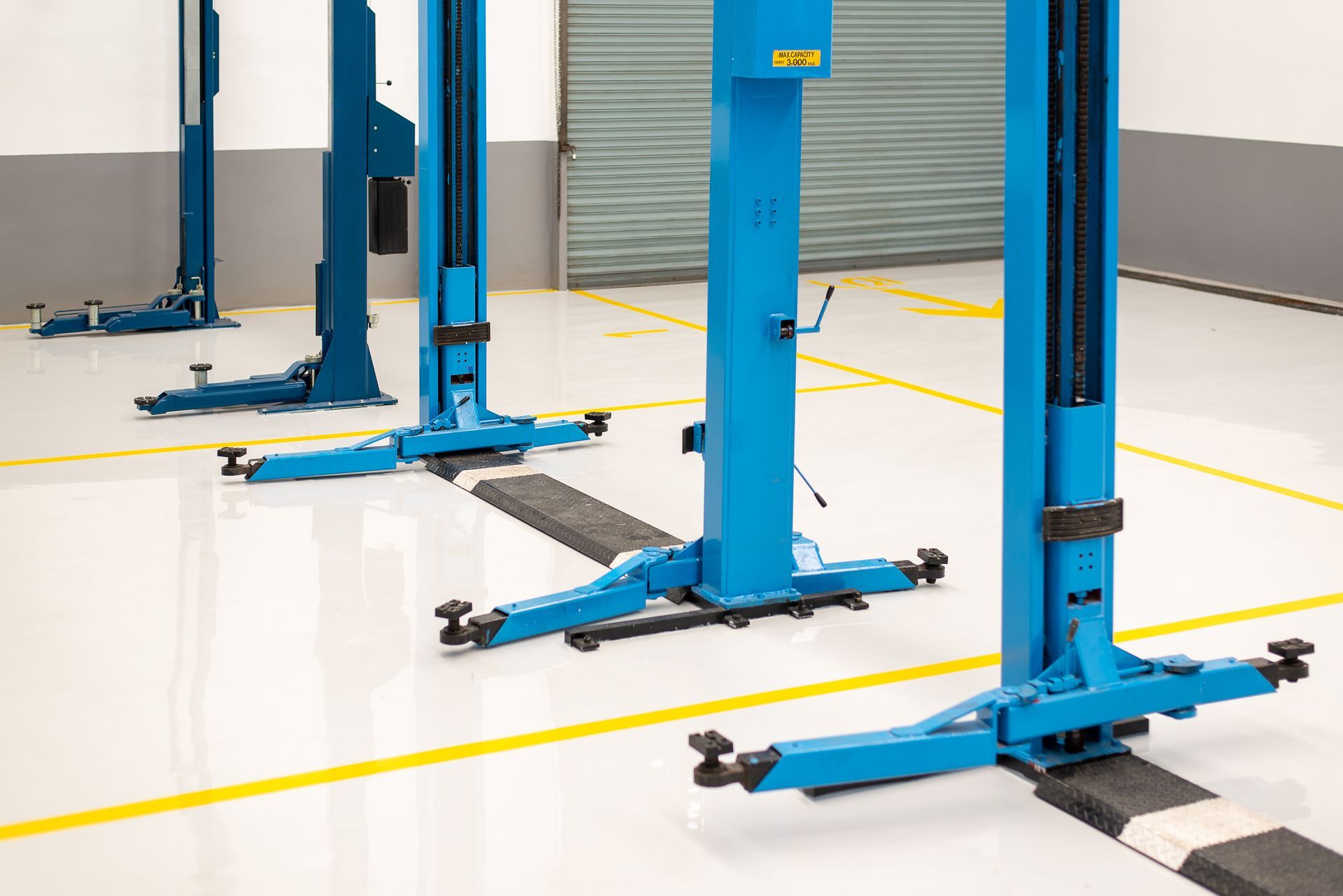 Several bright blue automotive lifts installed in a clean, professional garage with yellow floor markings.