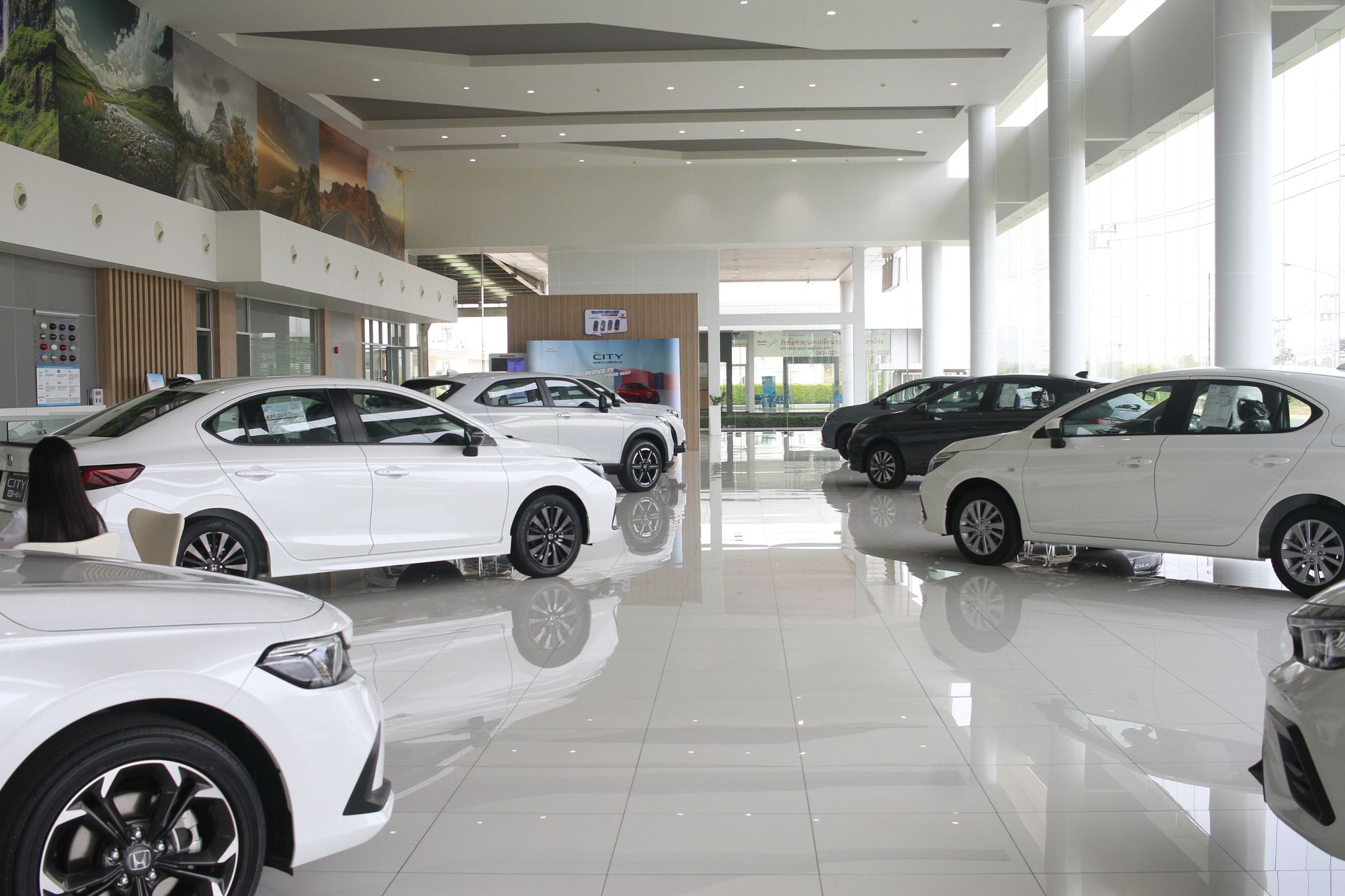 A car dealership showroom with rows of white and dark colored vehicles parked on a polished, reflective floor.