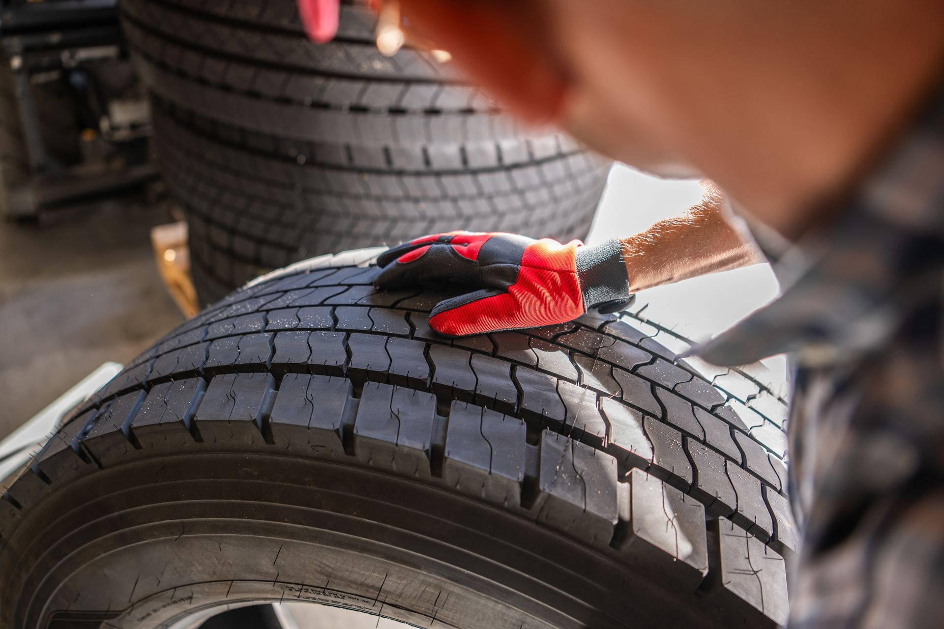 A mechanic wearing red and black work gloves inspects the tread of a tire in a shop.
