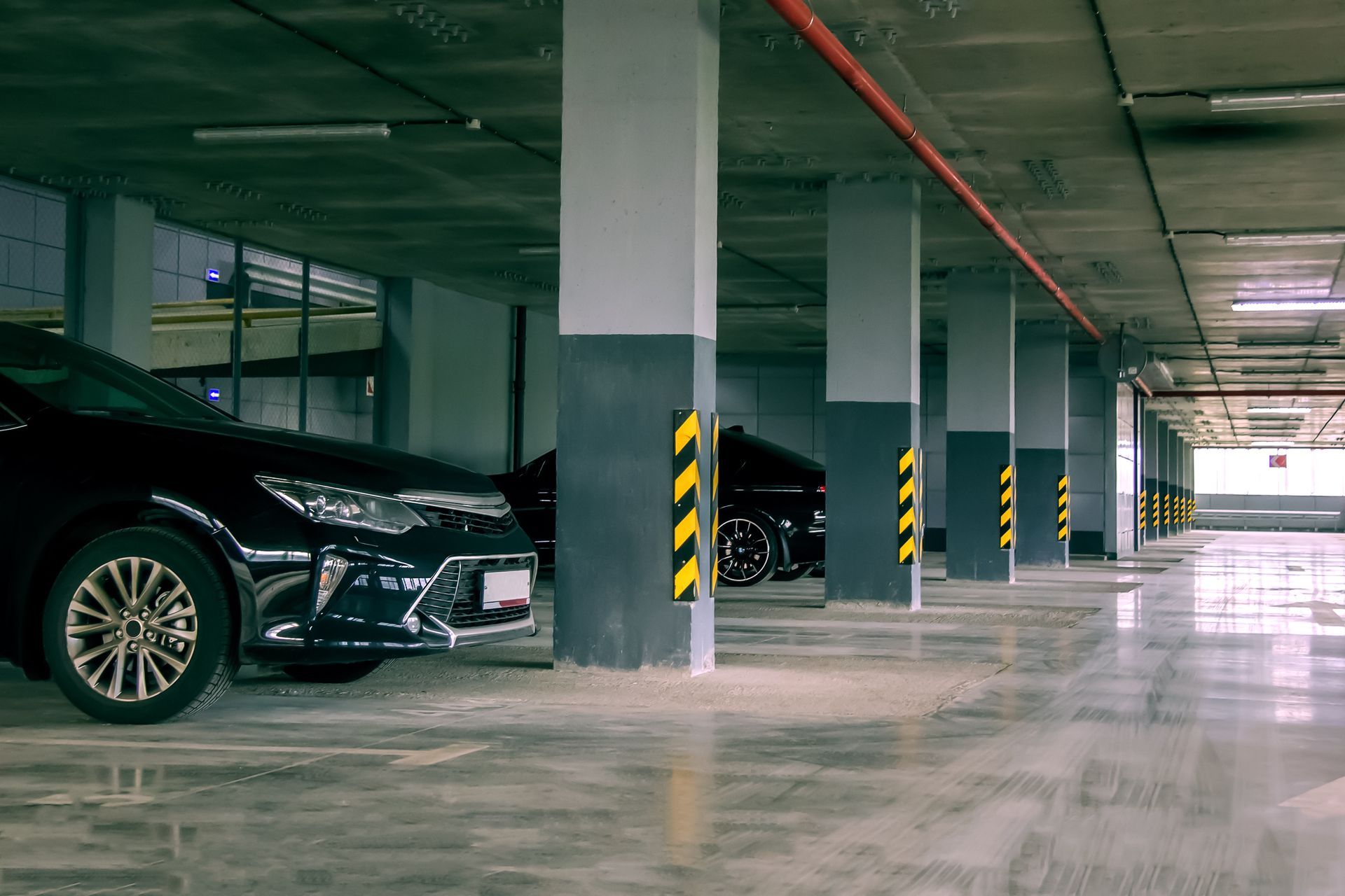 A row of grey parking garage pillars with yellow and black safety tape, with parked cars visible on the left.