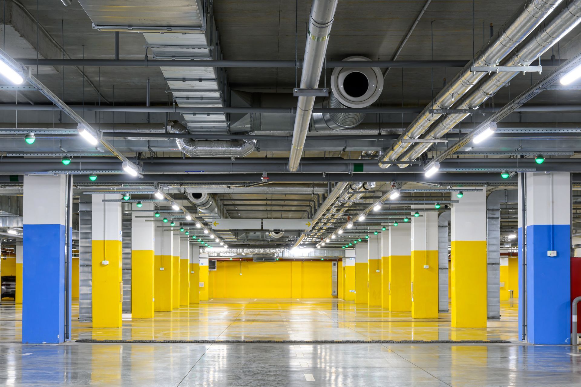 An indoor parking garage with concrete floors, white ceilings, and support pillars painted with blue and yellow accents.