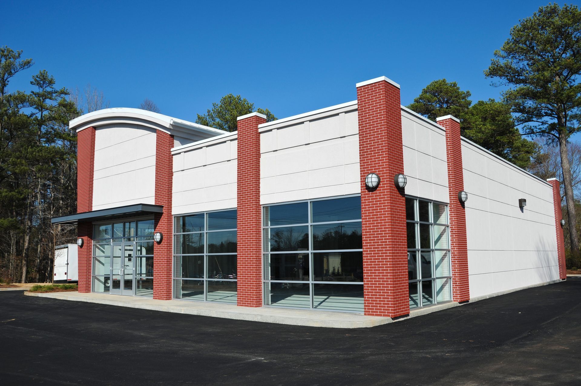A modern, white commercial building with red, patterned vertical columns and large glass windows under a clear blue sky.