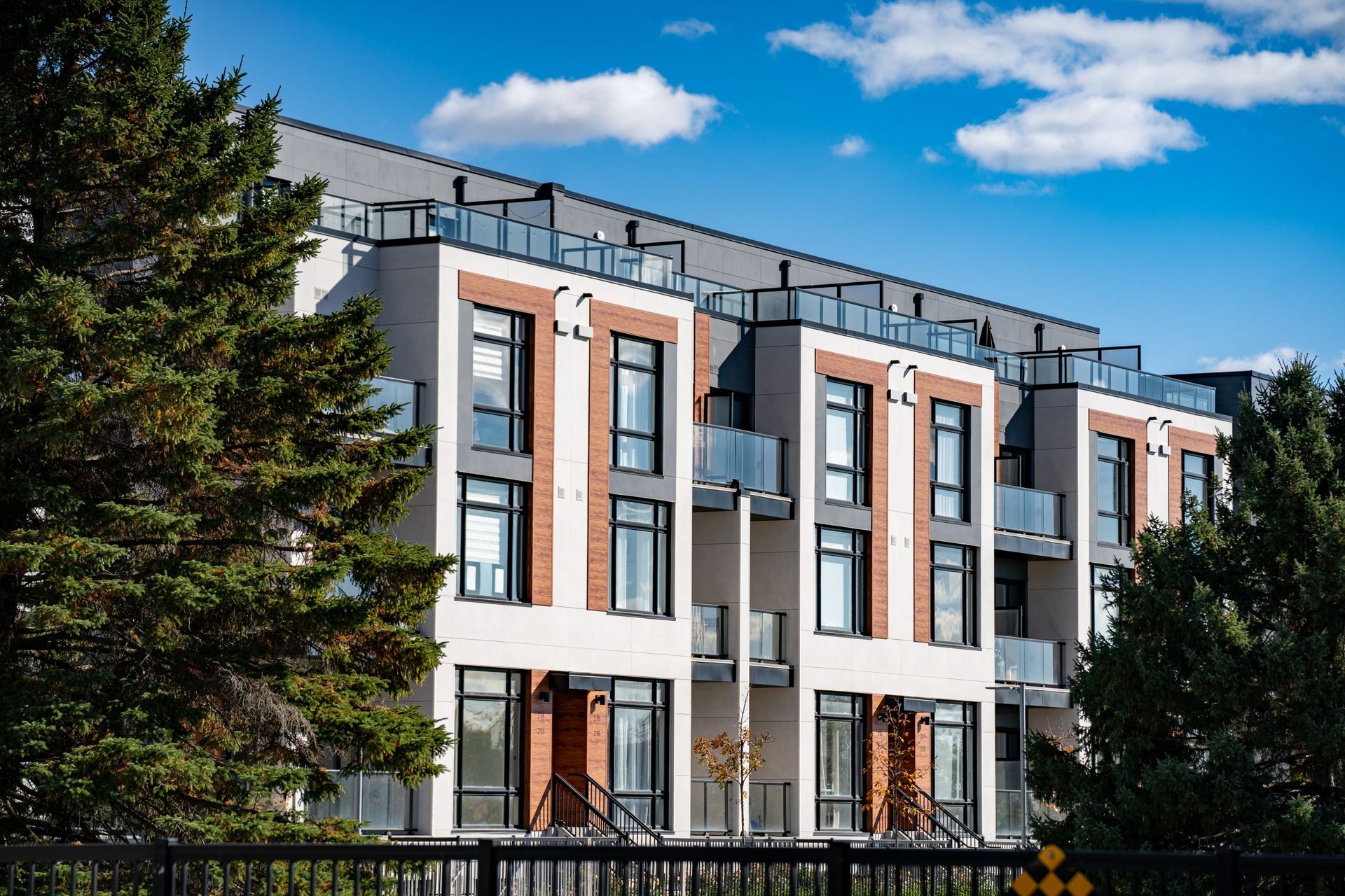 A modern multi-story residential townhouse complex with white stucco and brick accents against a clear blue sky.
