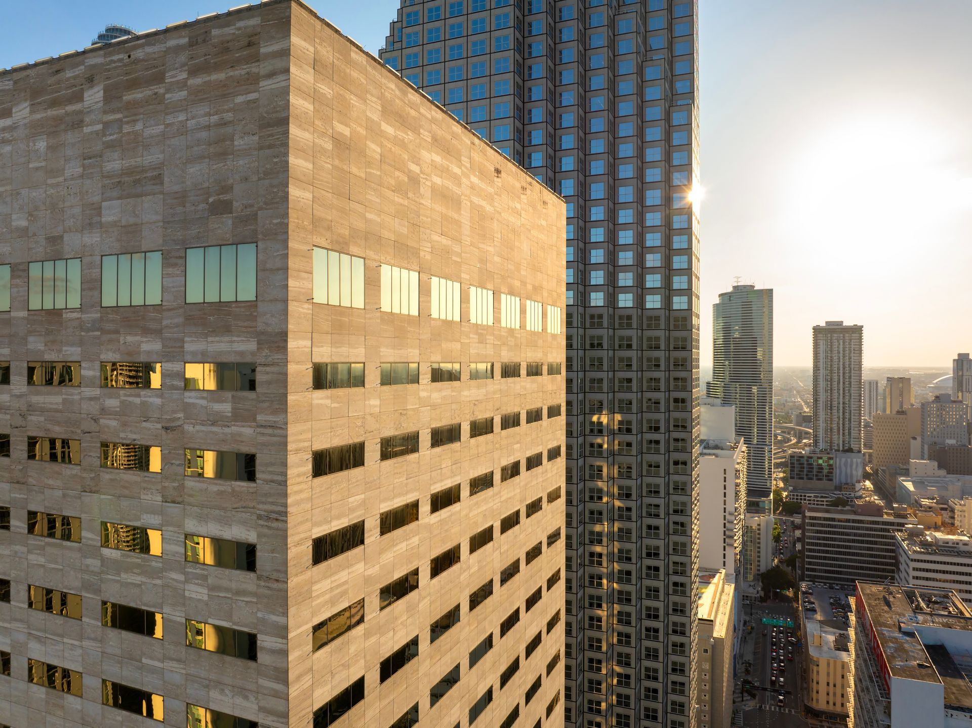 A stone-facade building in the foreground sits next to a glass skyscraper during a sunny, bright afternoon in a city.