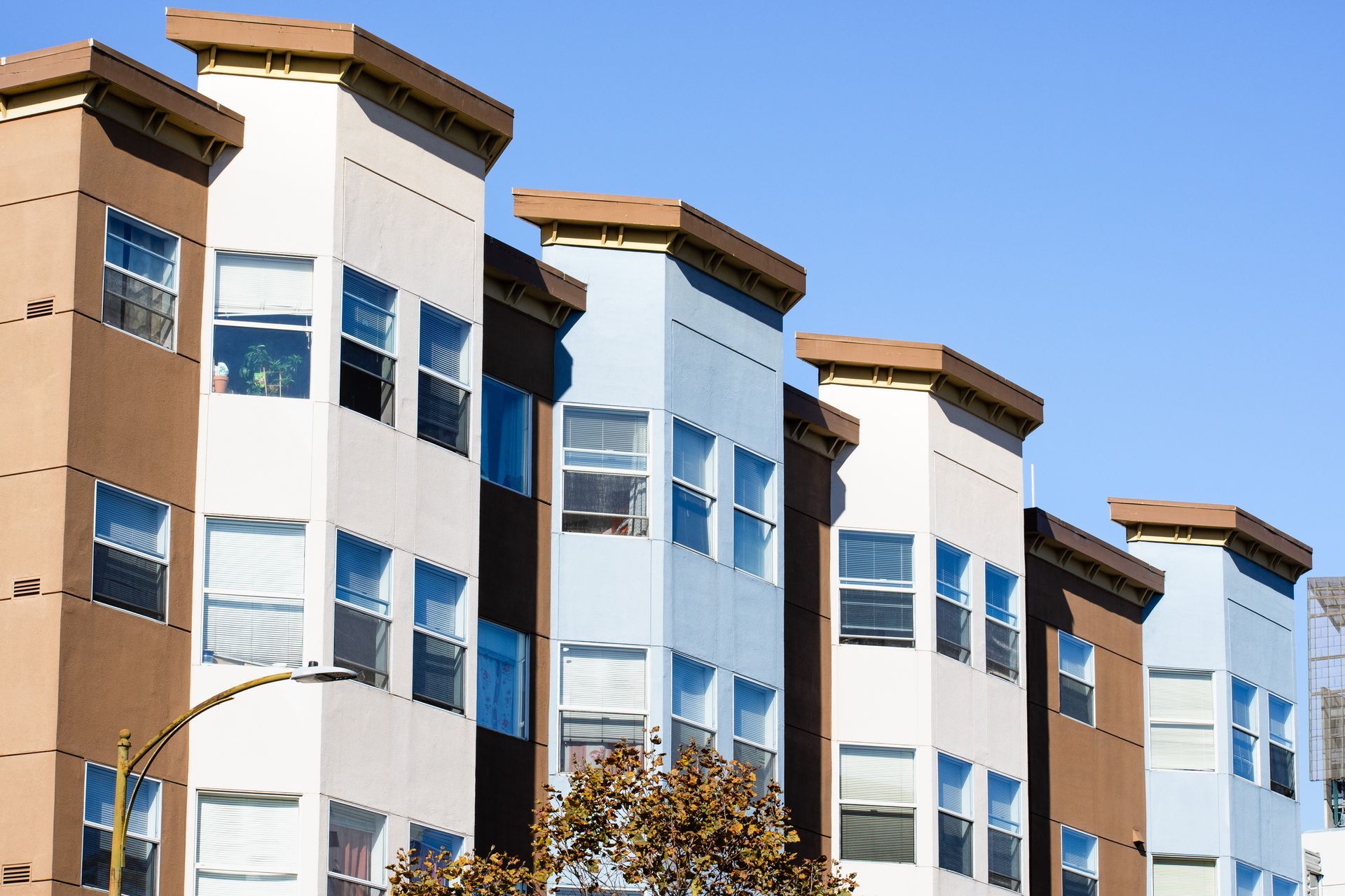 A low-angle view of modern multi-story apartment buildings with tan and light blue exterior facades against a clear sky.