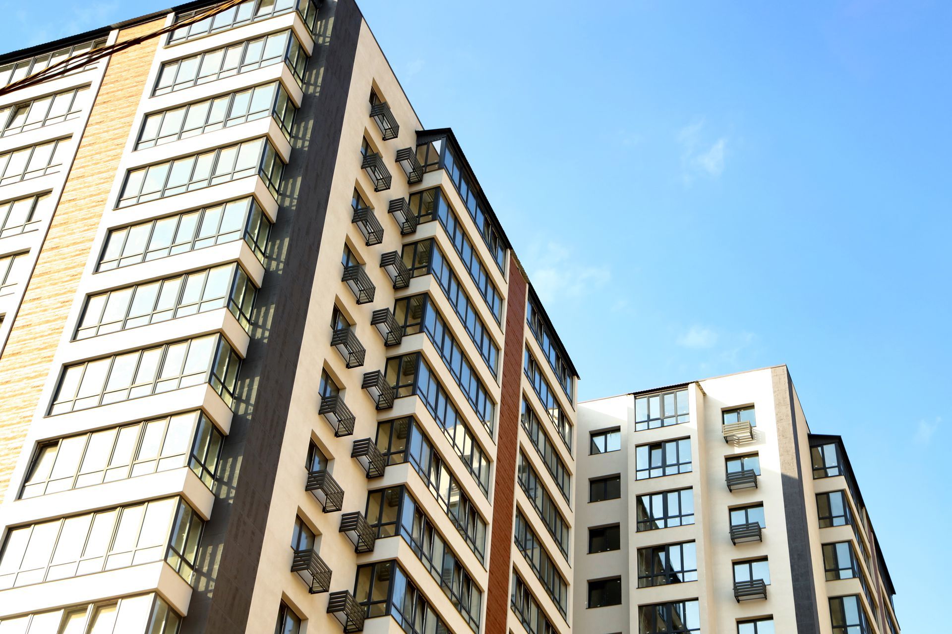 A low-angle view of modern, multi-story apartment buildings with balconies and glass windows against a blue sky.