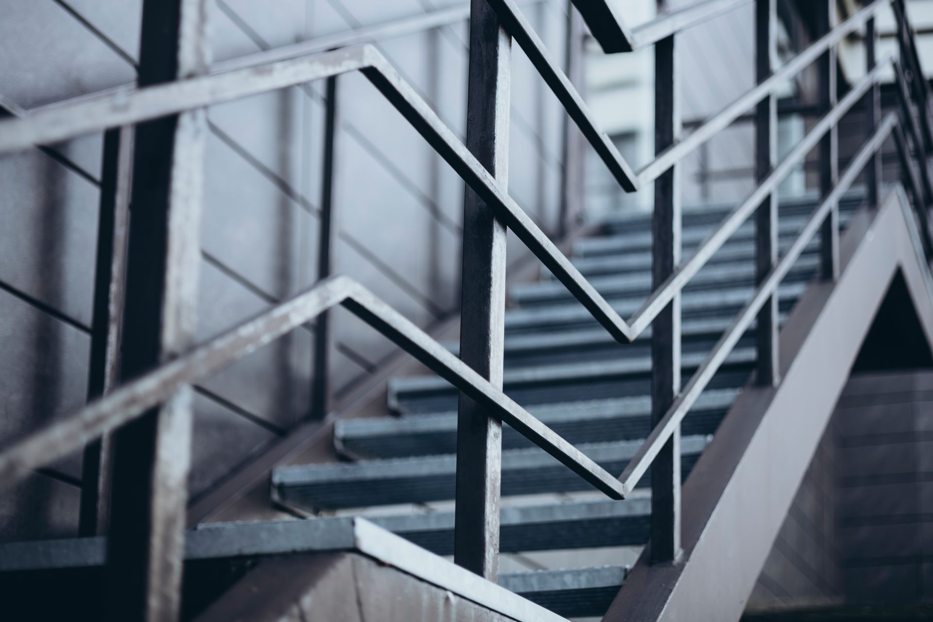 A low-angle view of an outdoor staircase with angular, zigzagging metal railings against a gray wall.