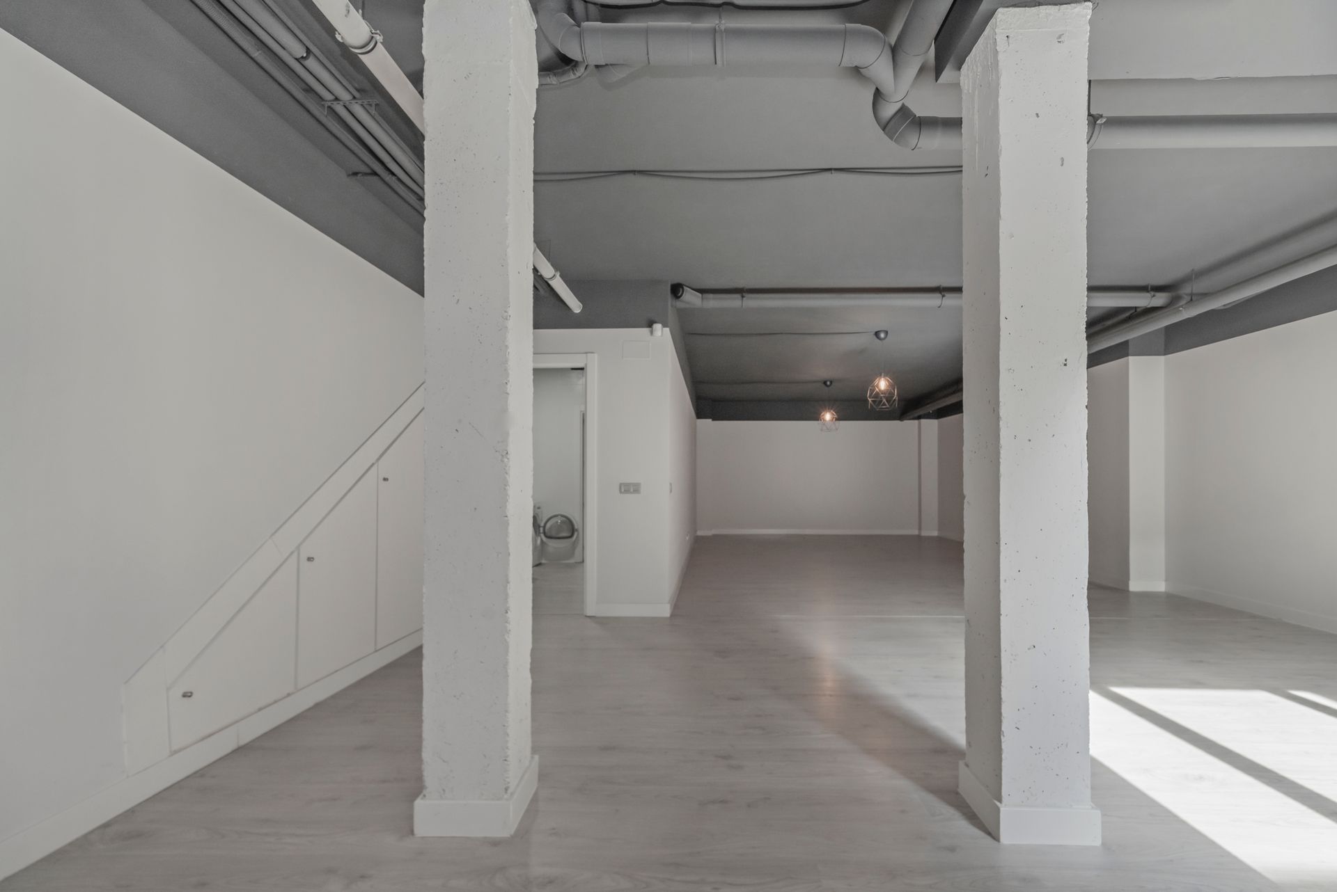 An empty, minimalist commercial space with white walls, two white pillars, and an industrial-style grey exposed ceiling.