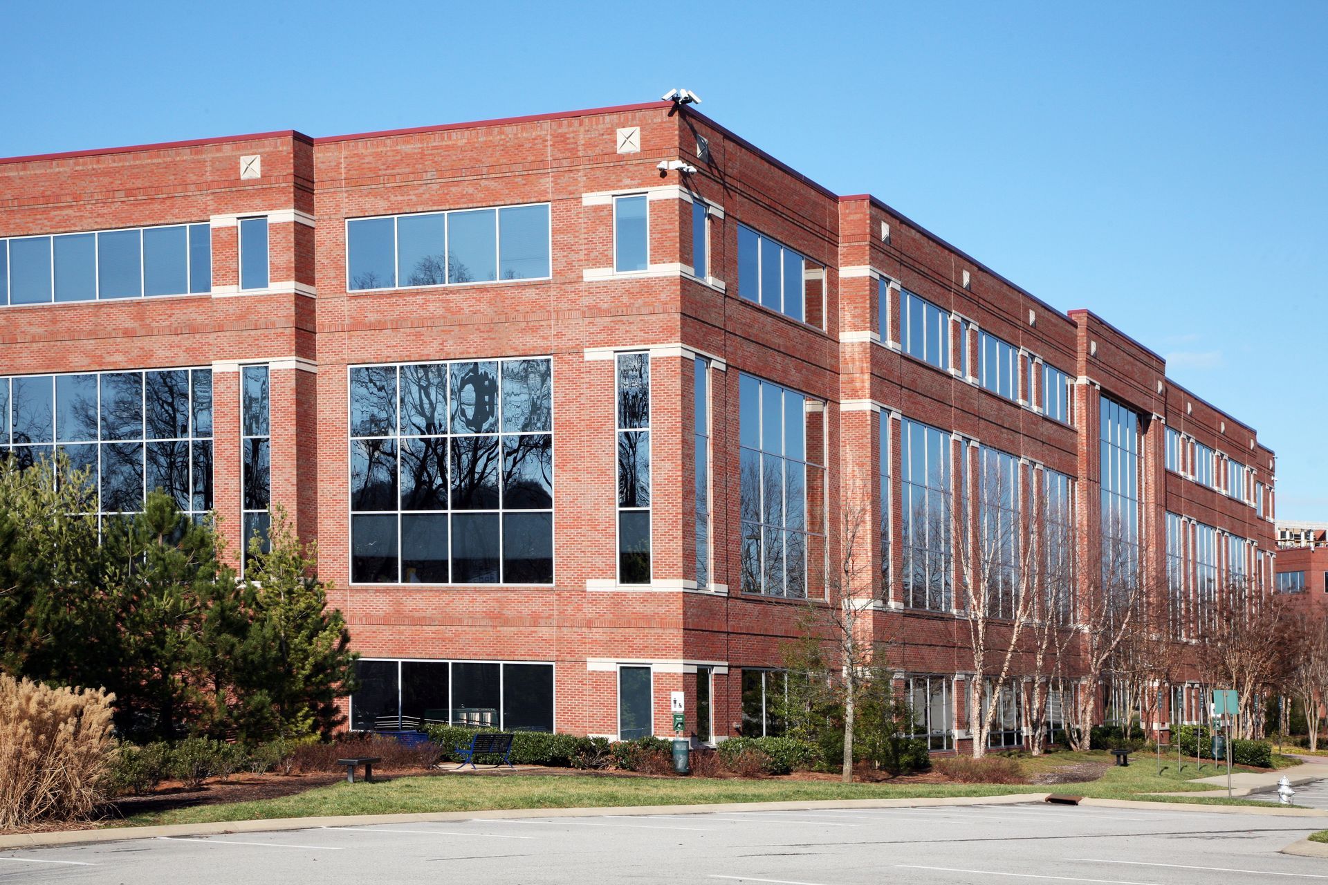 A modern, four-story red brick office building with large rectangular glass windows, set against a clear blue sky.