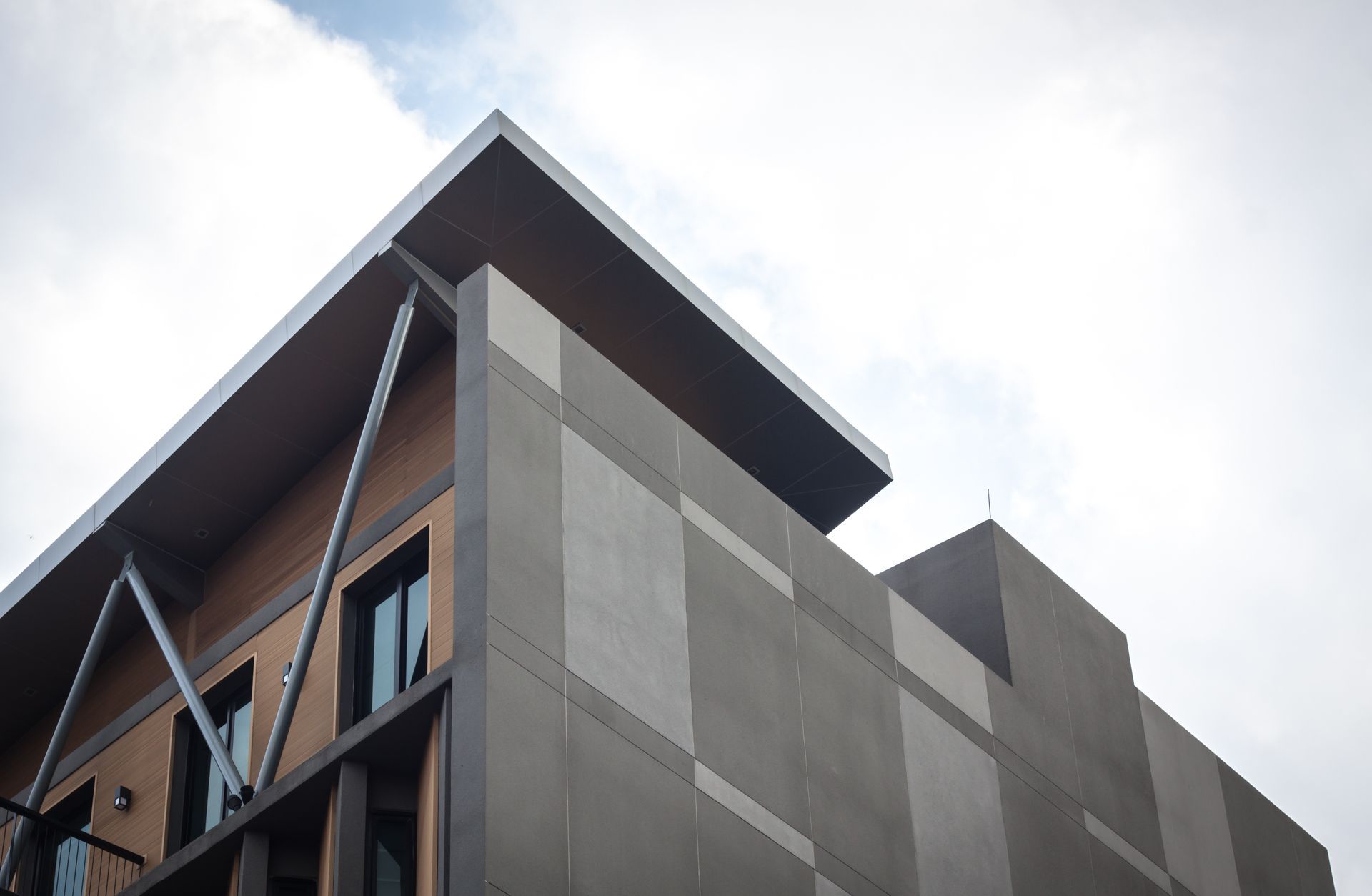A low-angle view of a modern building featuring a sharp roofline, gray concrete panels, and dark wood siding.