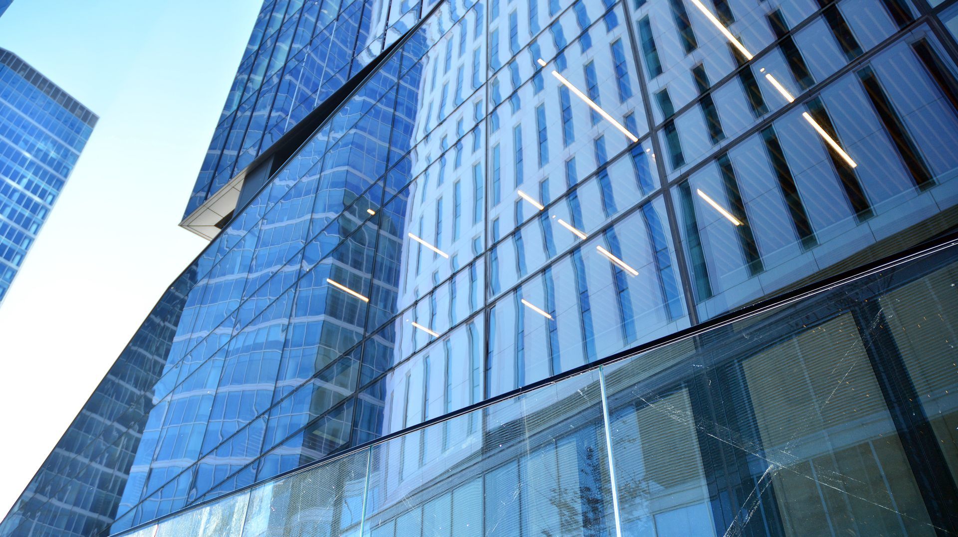 A low-angle view of a modern glass skyscraper with geometric blue panels and reflective windows under a clear sky.