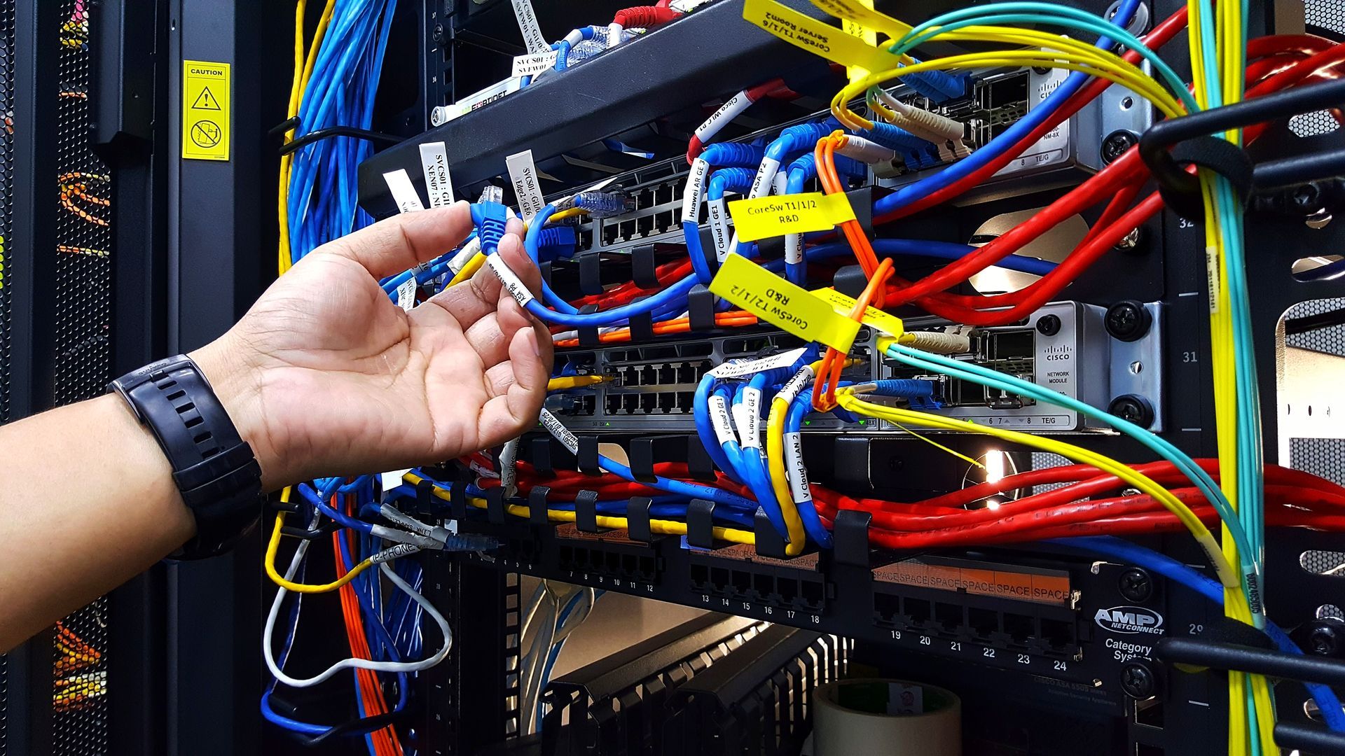 A person’s hand adjusting blue ethernet cables on a server rack filled with colorful wiring.