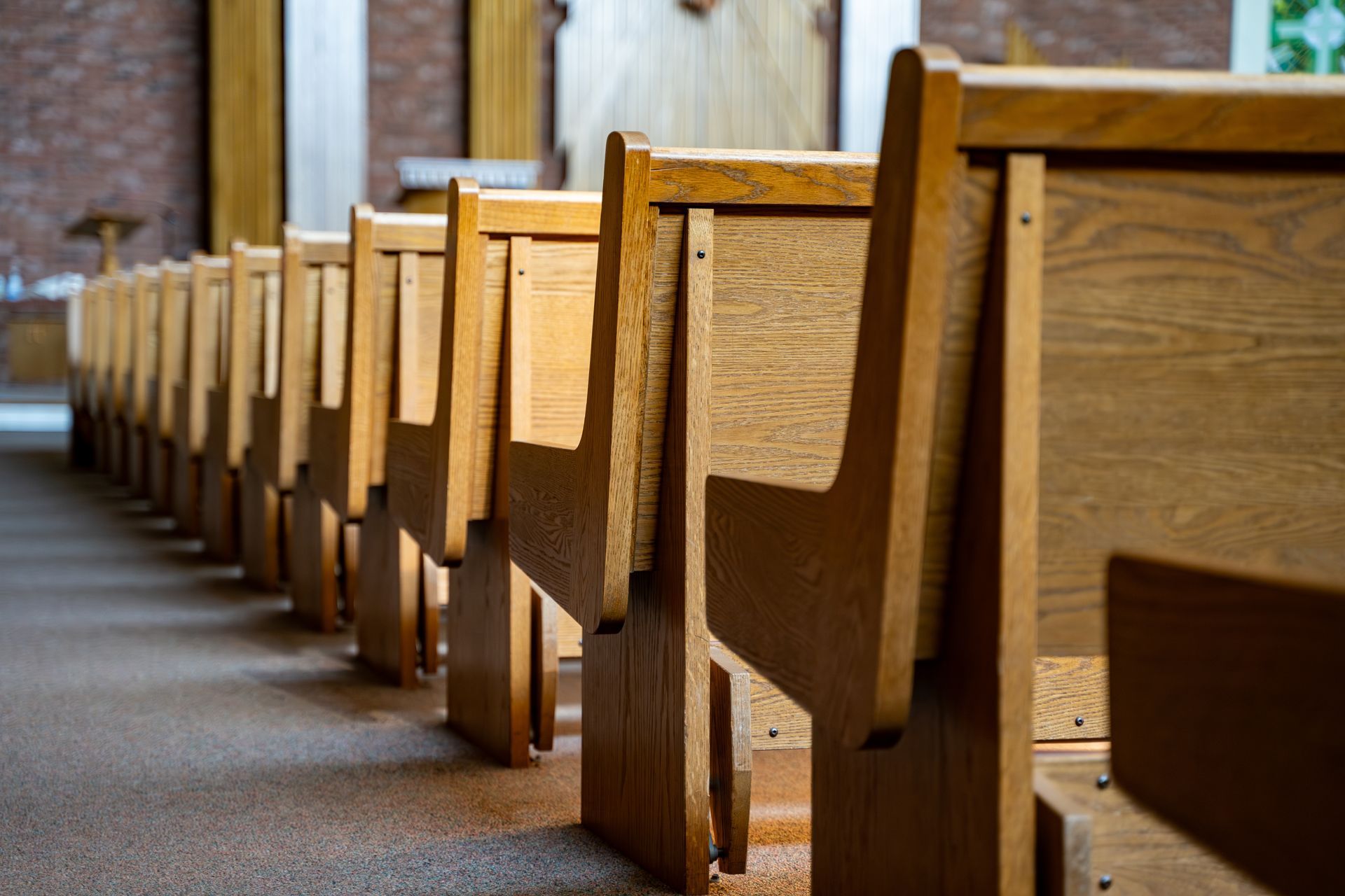 A row of wooden church pews in a sanctuary, angled toward the front, with a brick wall in the background.