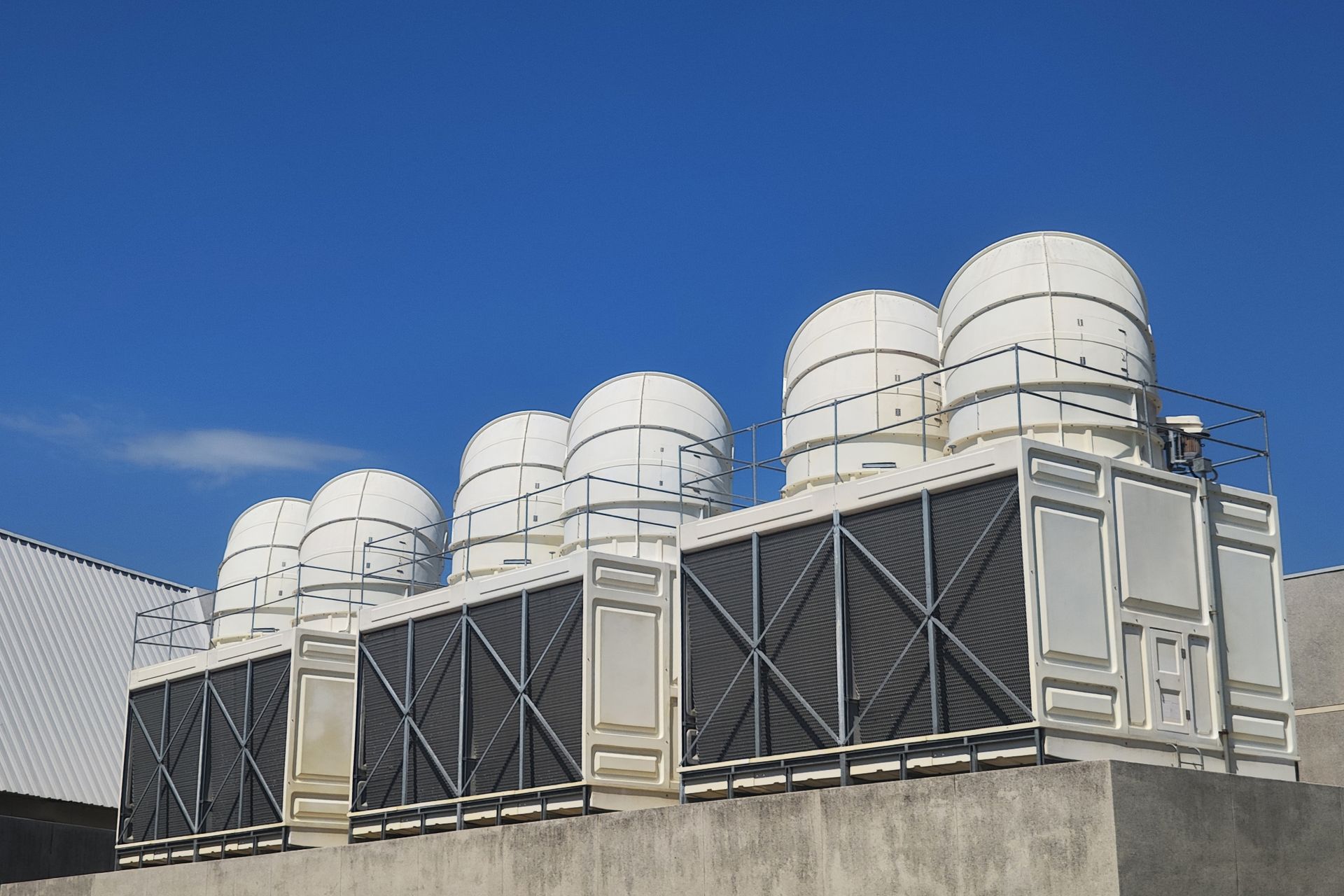 A row of large, white industrial cooling towers with dark, cross-hatched metal grilles against a clear blue sky.