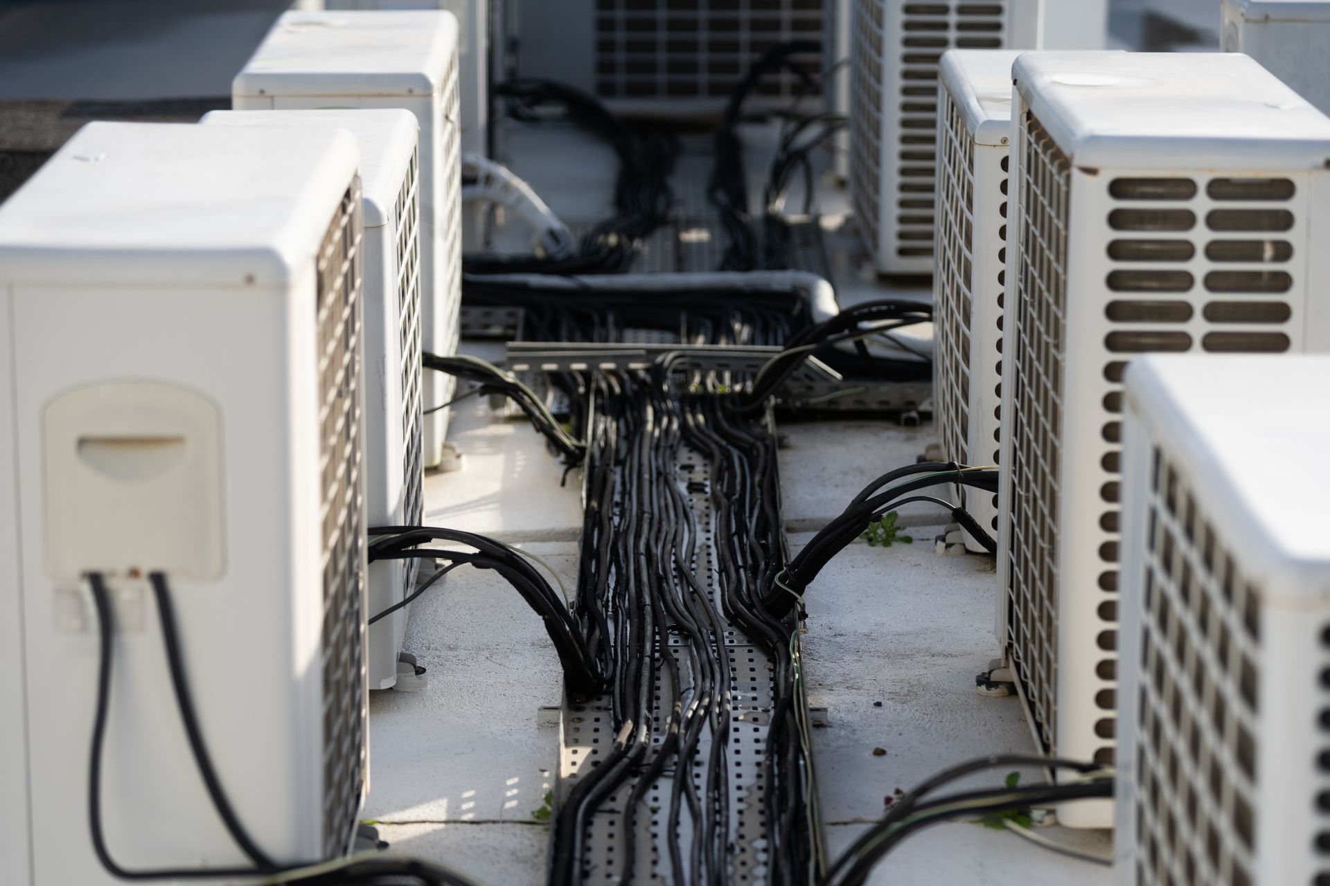 Multiple outdoor air conditioning units on a rooftop, with a central metal cable tray organizing black electrical wires.