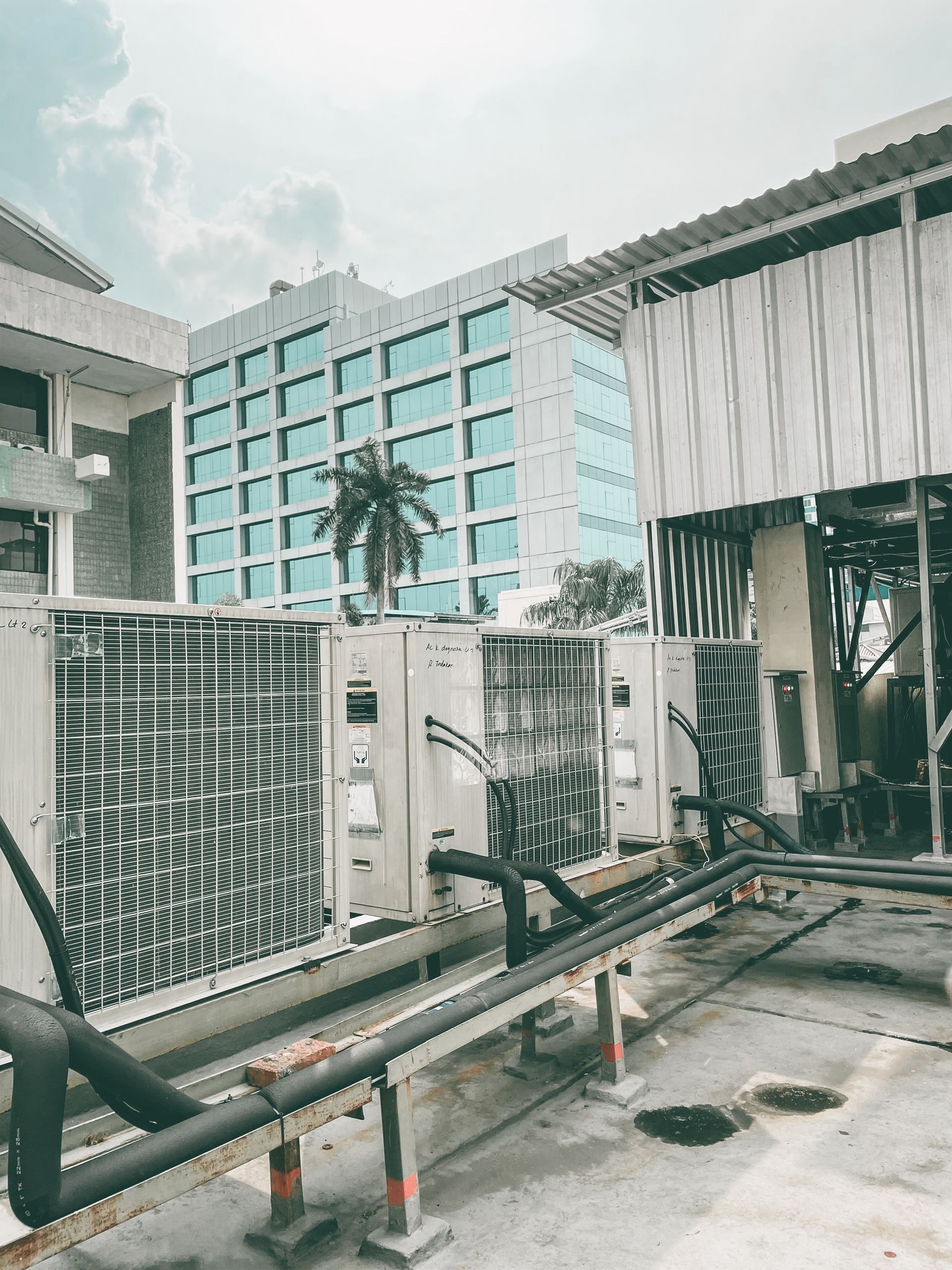 Industrial air conditioning units installed on a rooftop terrace against the backdrop of a modern glass office building.