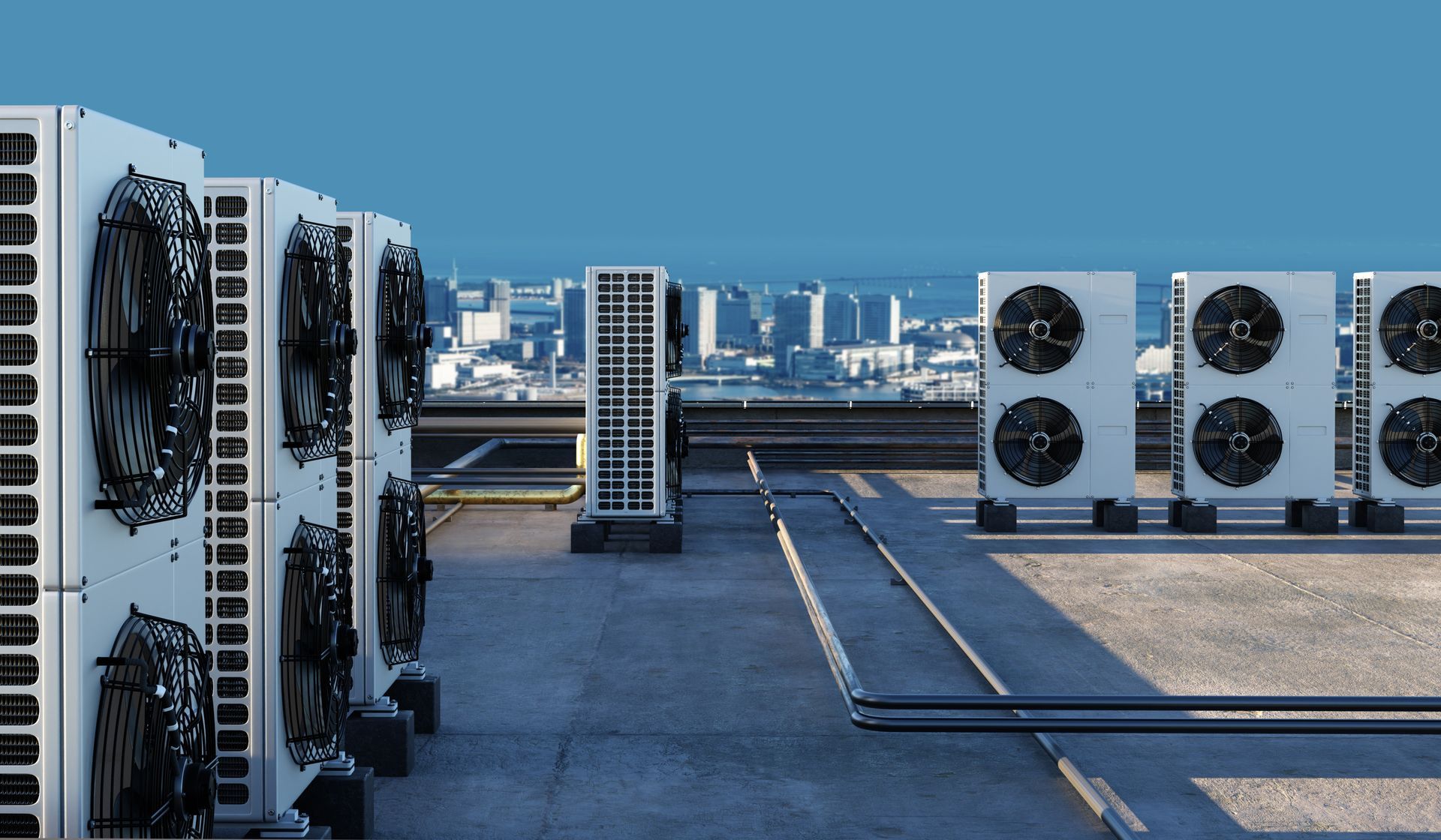 Several white commercial air conditioning units arranged on a rooftop, with a blurry cityscape in the background.