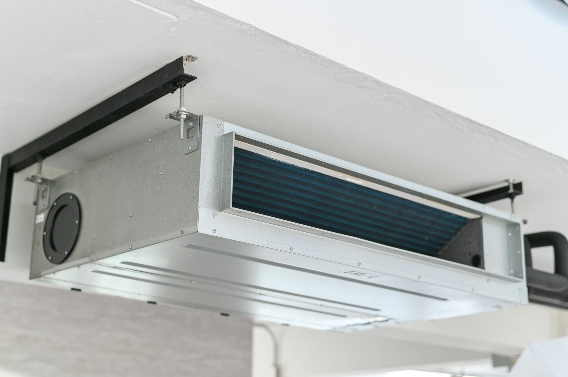 A ceiling-mounted ducted air conditioning unit installed with metal brackets against a white ceiling.
